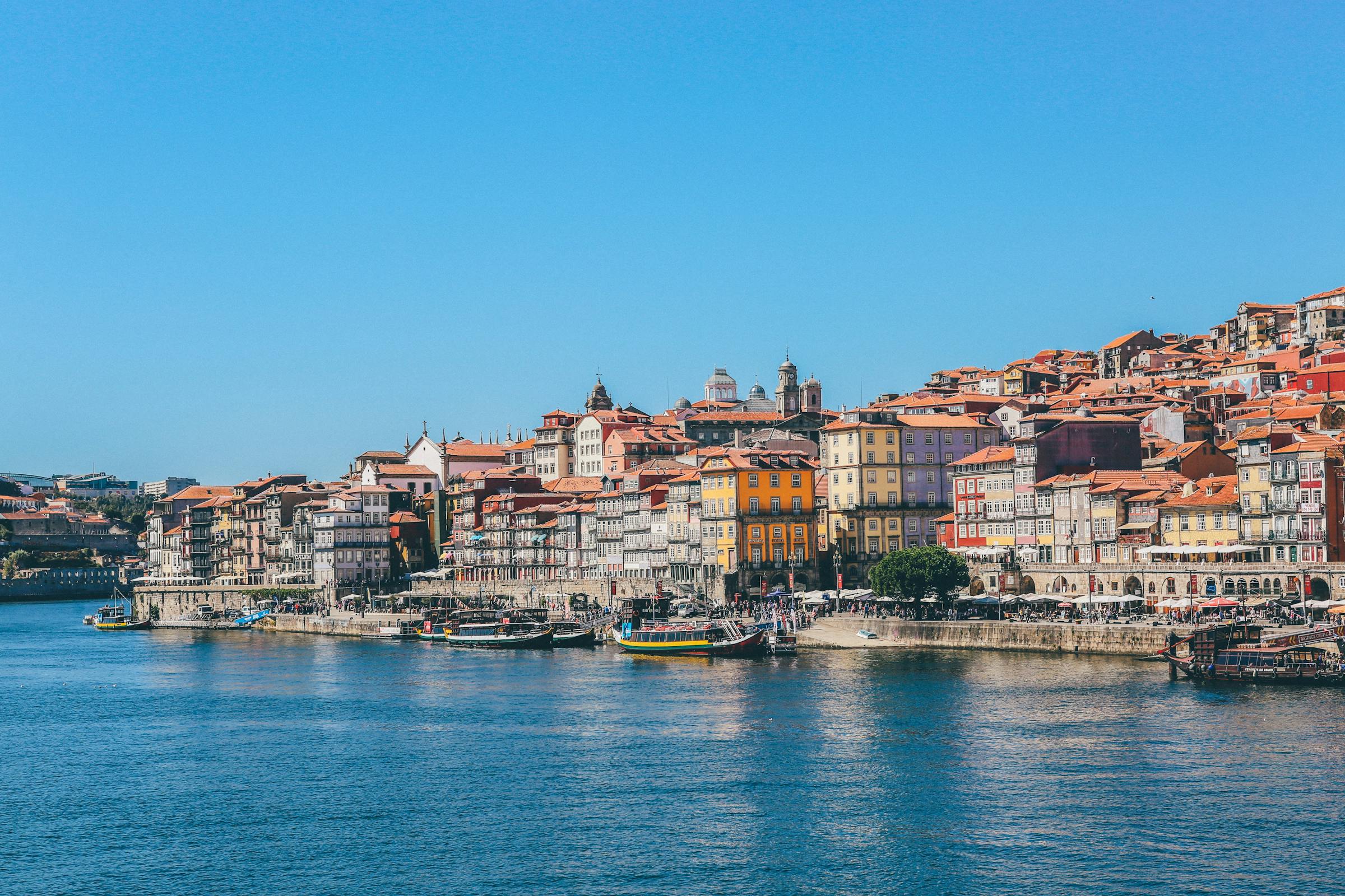 Colourful houses of Porto's Ribeira district line the Douro River, with boats moored along the waterfront.