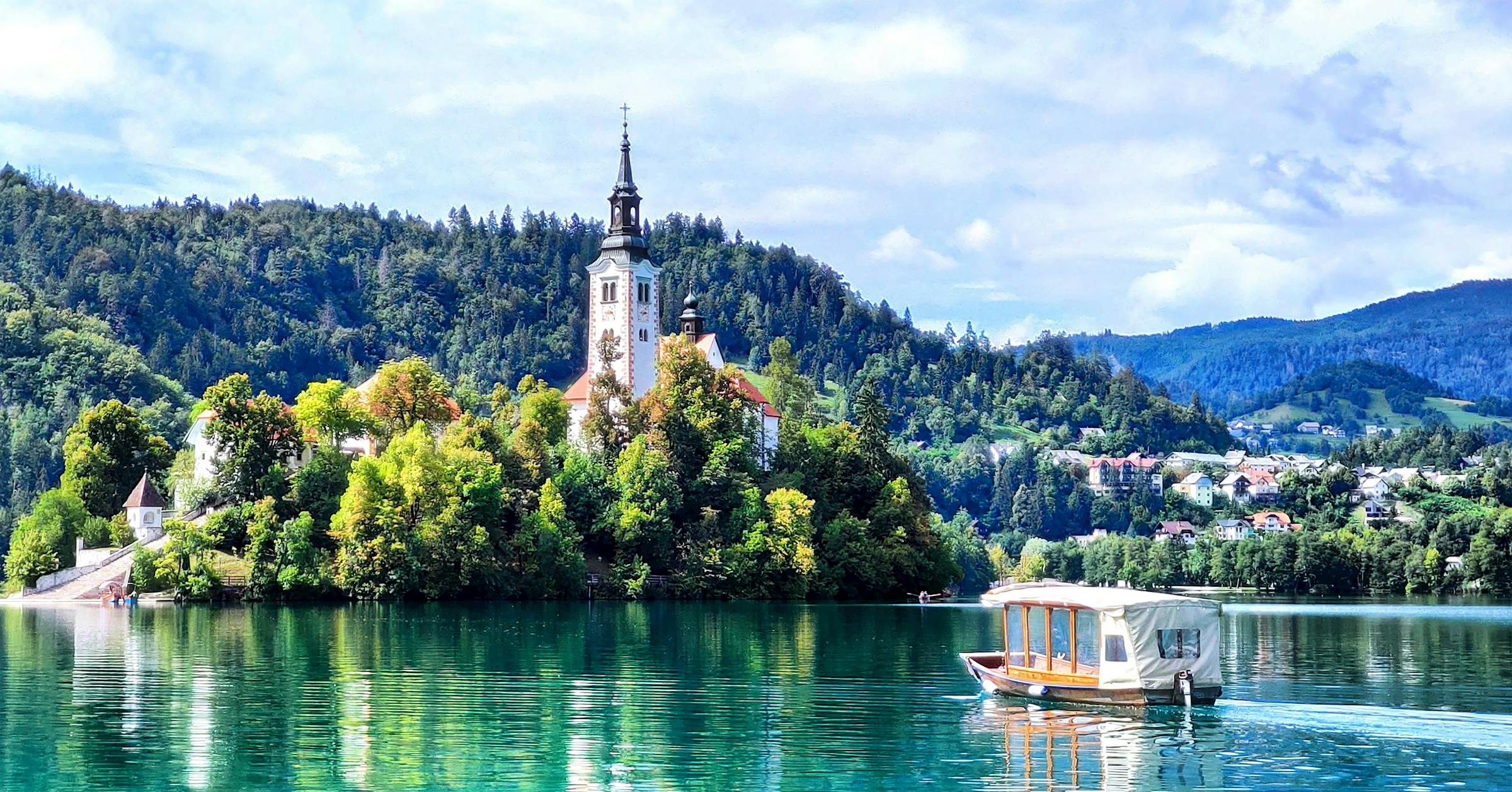 A wooden boat crosses Lake Bled toward the island church's white bell tower, Slovenia.