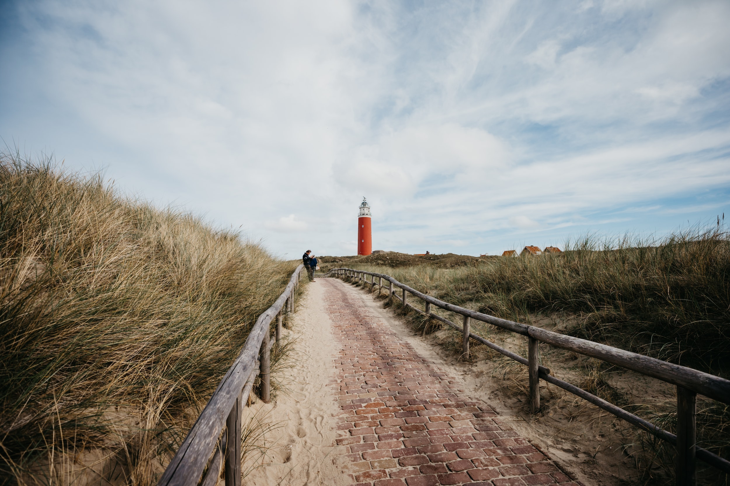 brown wooden pathway between green grass field under white clouds during daytime