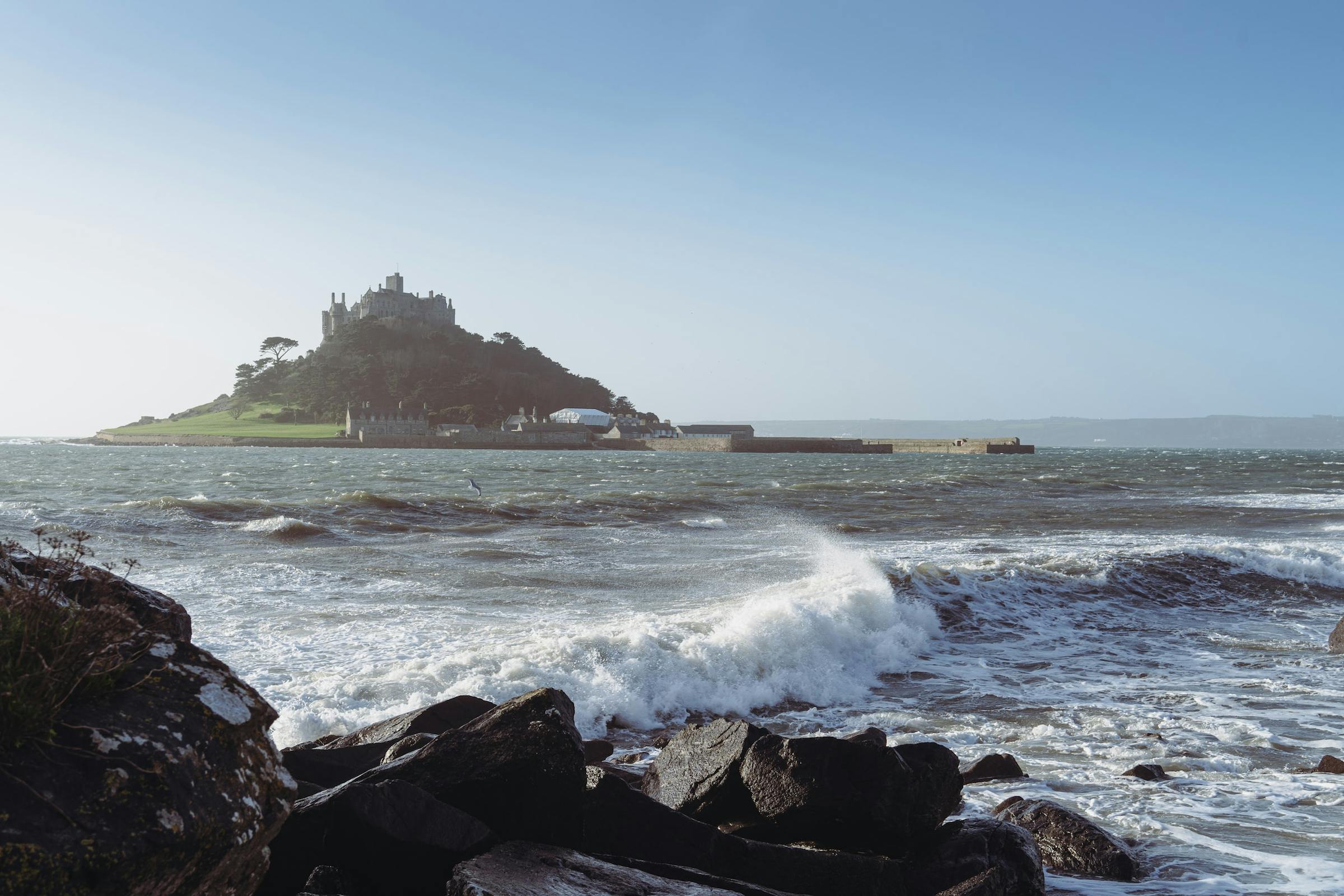 St Michael's Mount rises from the sea off Penzance, with waves breaking over rocks nearby.