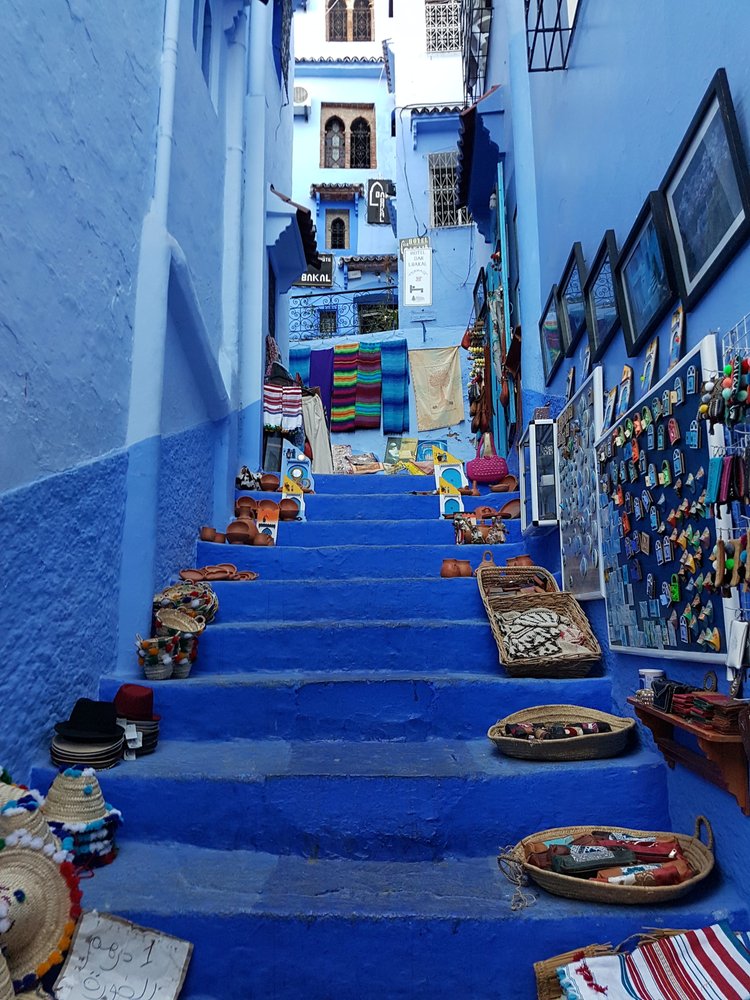 blue stairs between blue houses with wares on the side, a hilly street in Morocco