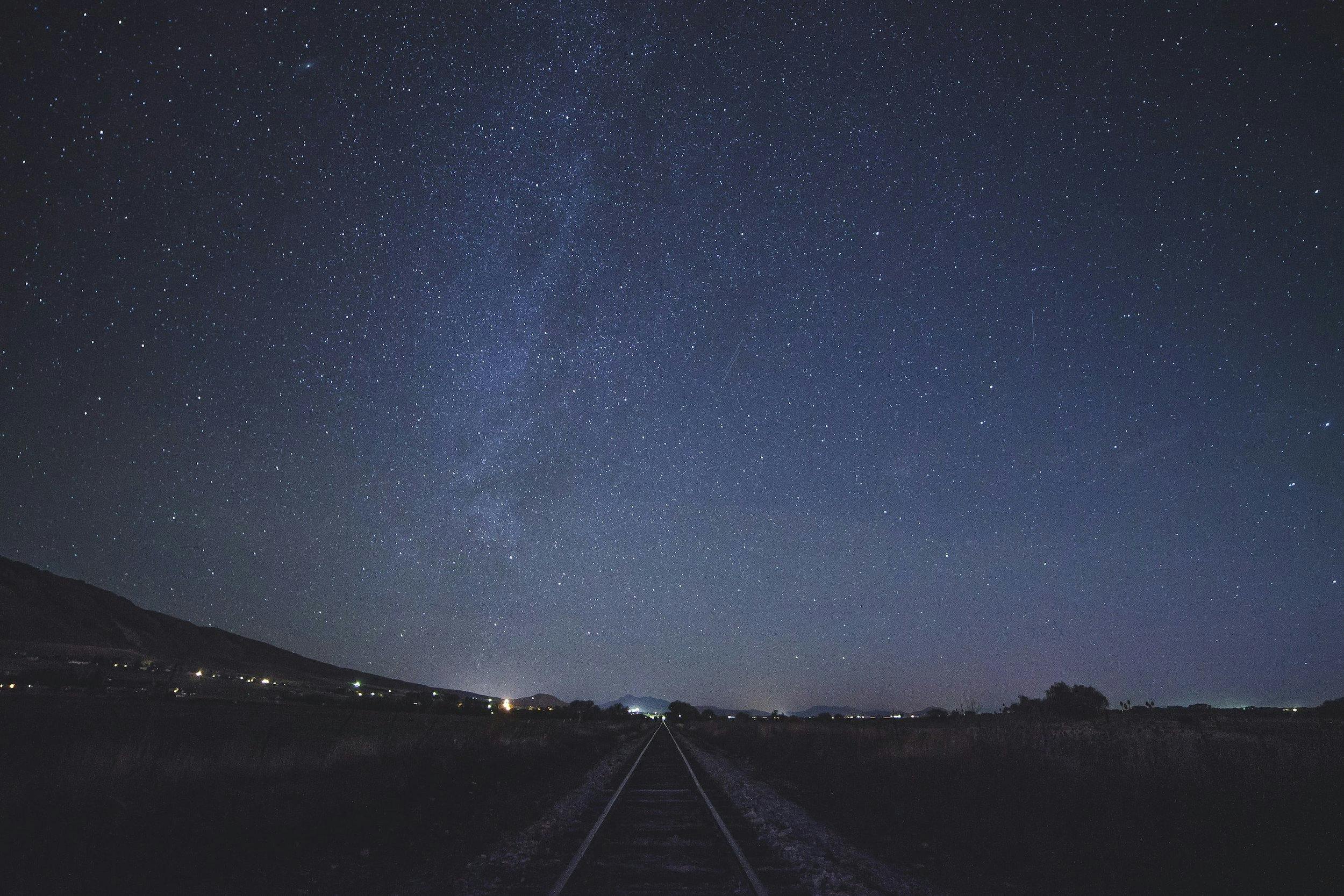 A starry sky at night, with a train track going into the distance
