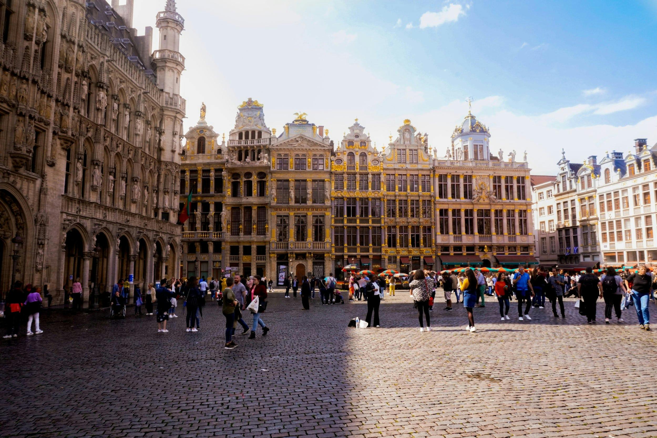 The Grand Place square in Brussels, visited by train. People walk around the square, admiring the old Baroque guildhalls and large town hall.