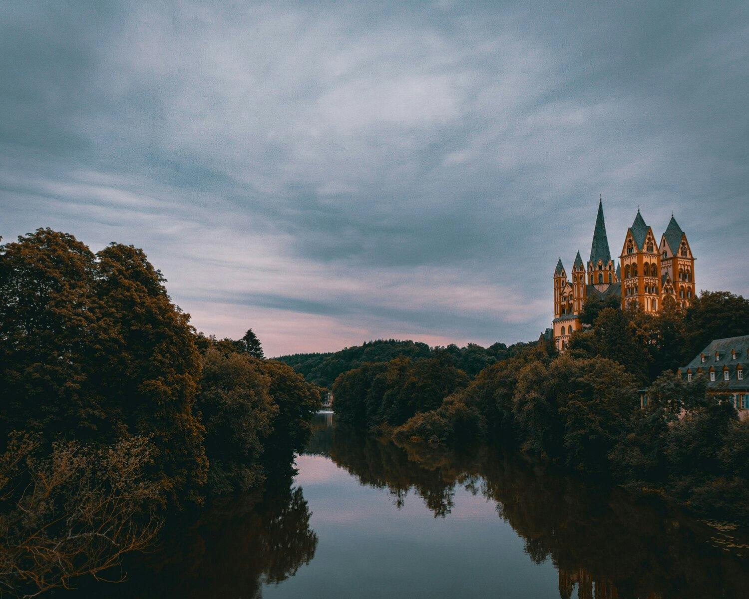 a view of the river Rhine in Germany with trees on each side, and a lit up castle with 5 turrets in the background