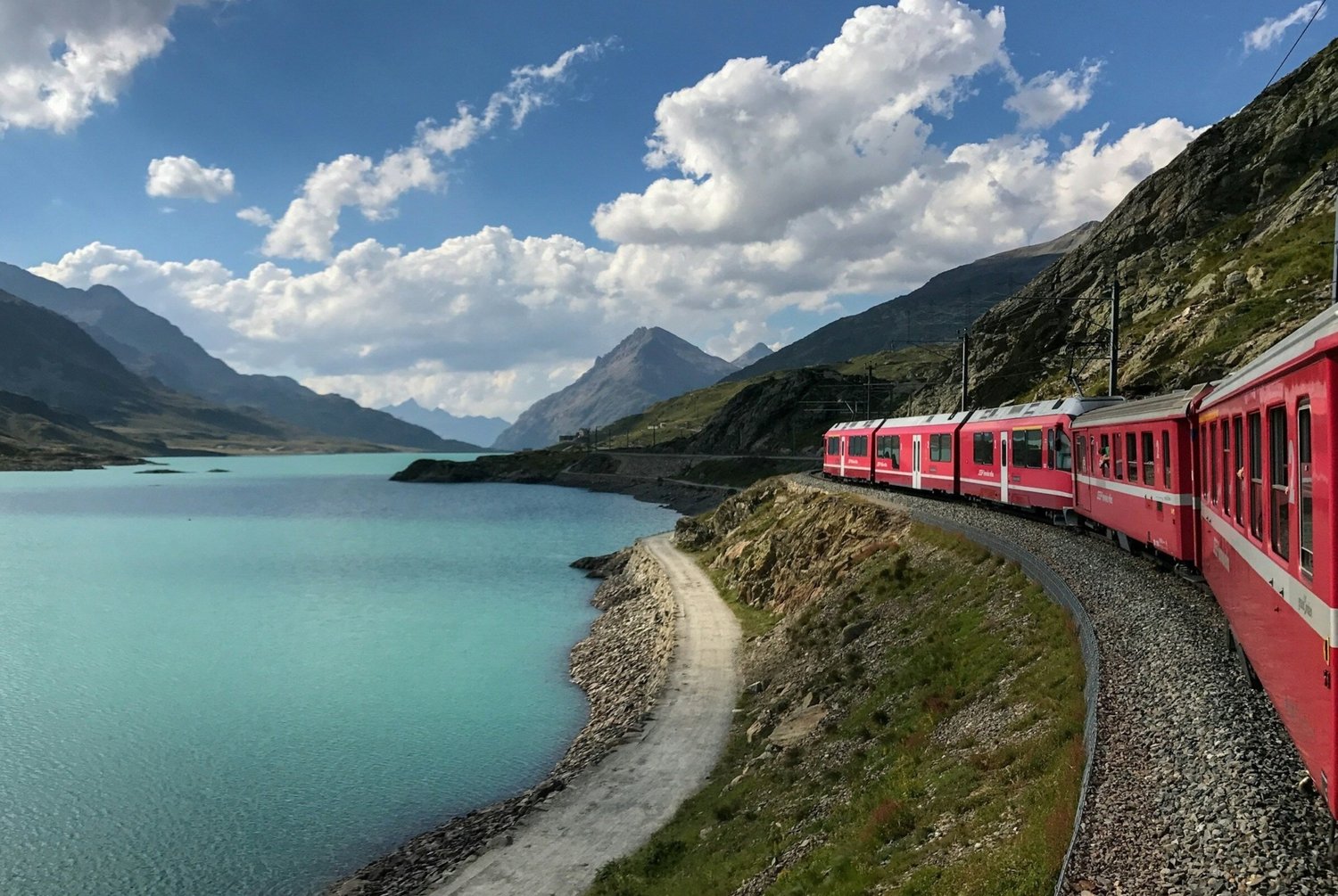 A view from the Rhaetian railway on the Bernina pass route, out of the train window, of the glacial azure lake on the left and the Swiss mountains in the background.
