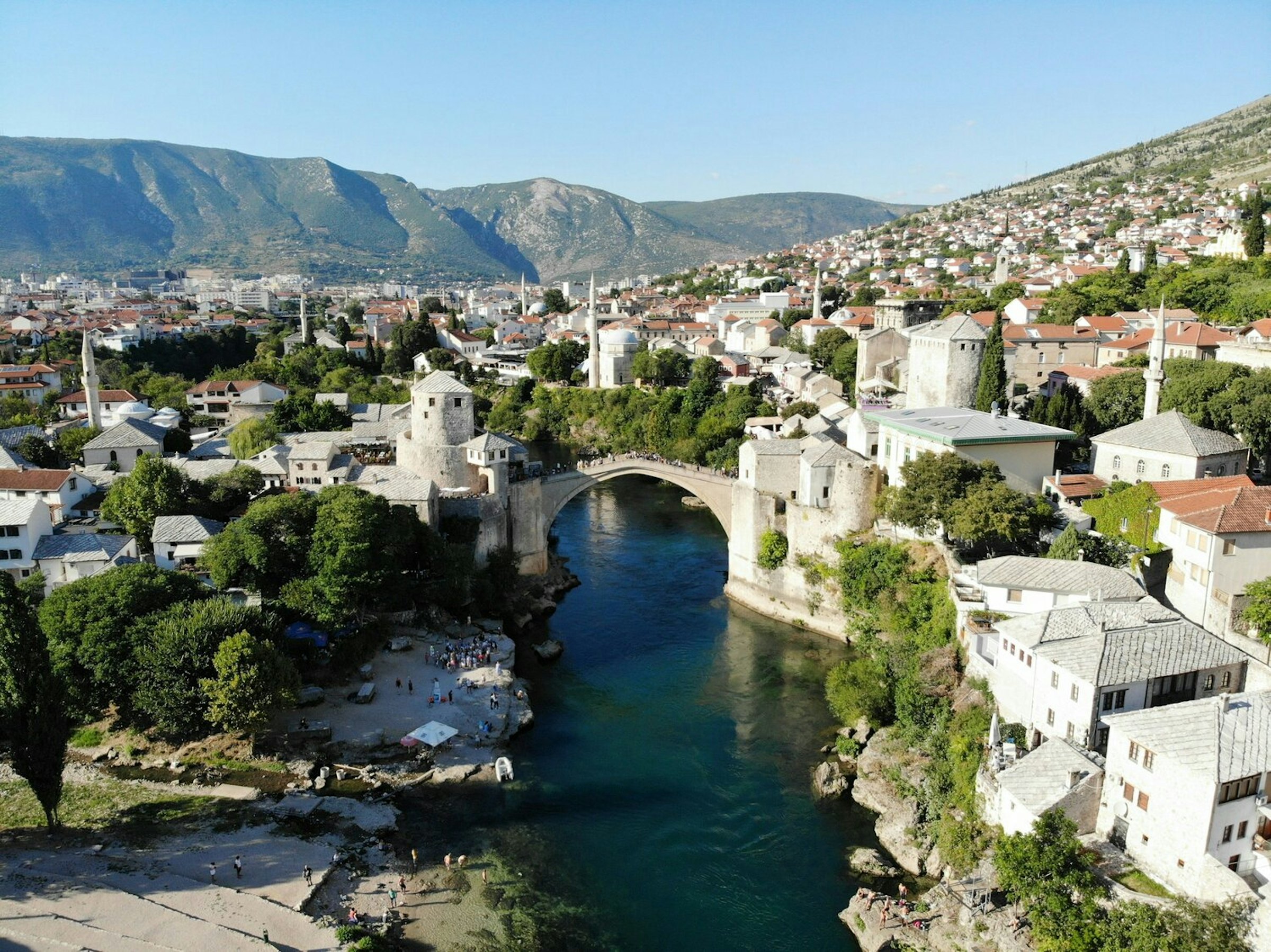 Mostar's Old Bridge arches over the turquoise Neretva river, old town and mountains behind, Bosnia