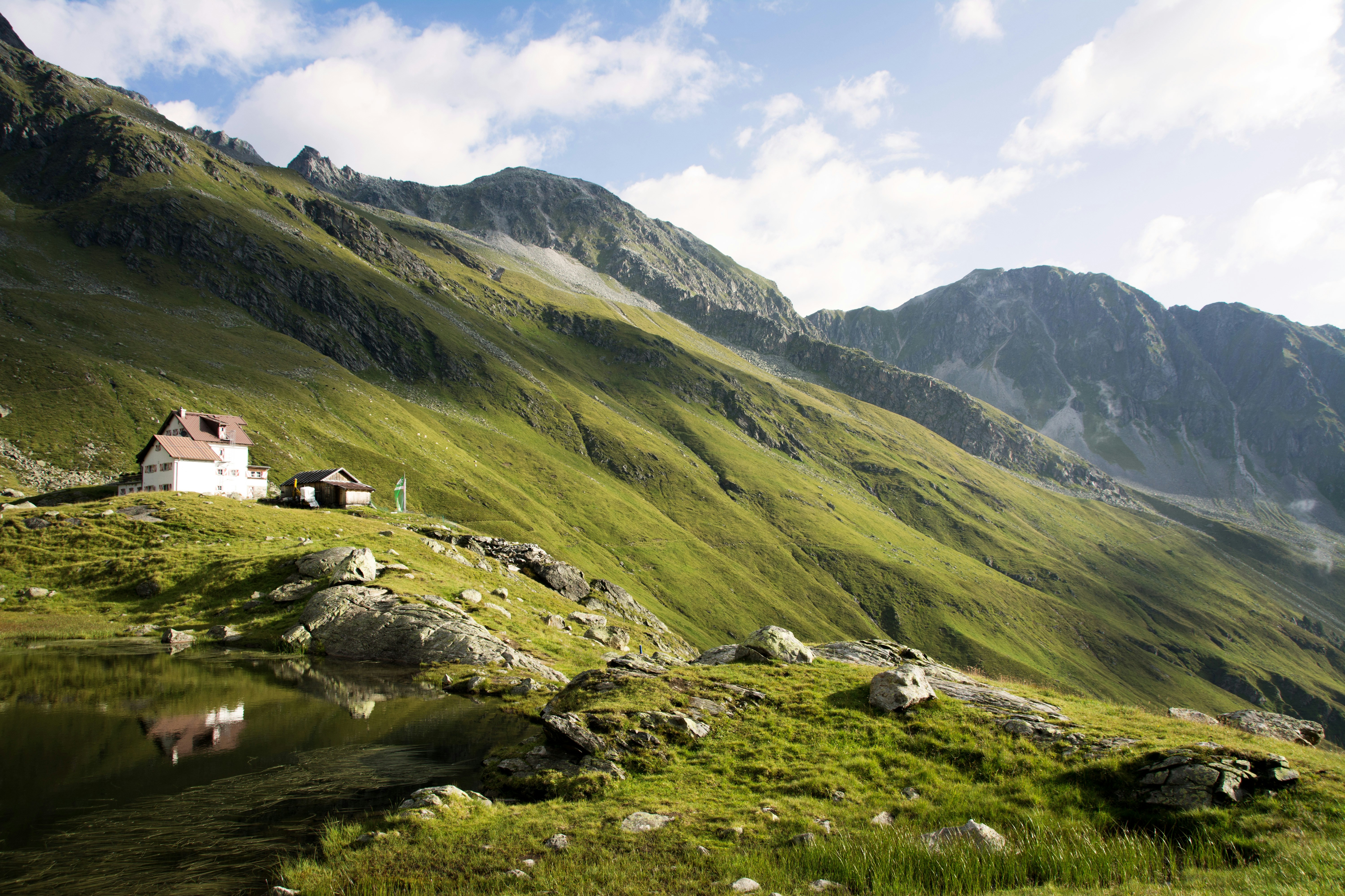 Green verdant mountainside in Austria, with one white house and shed standing alone in the middle of it.