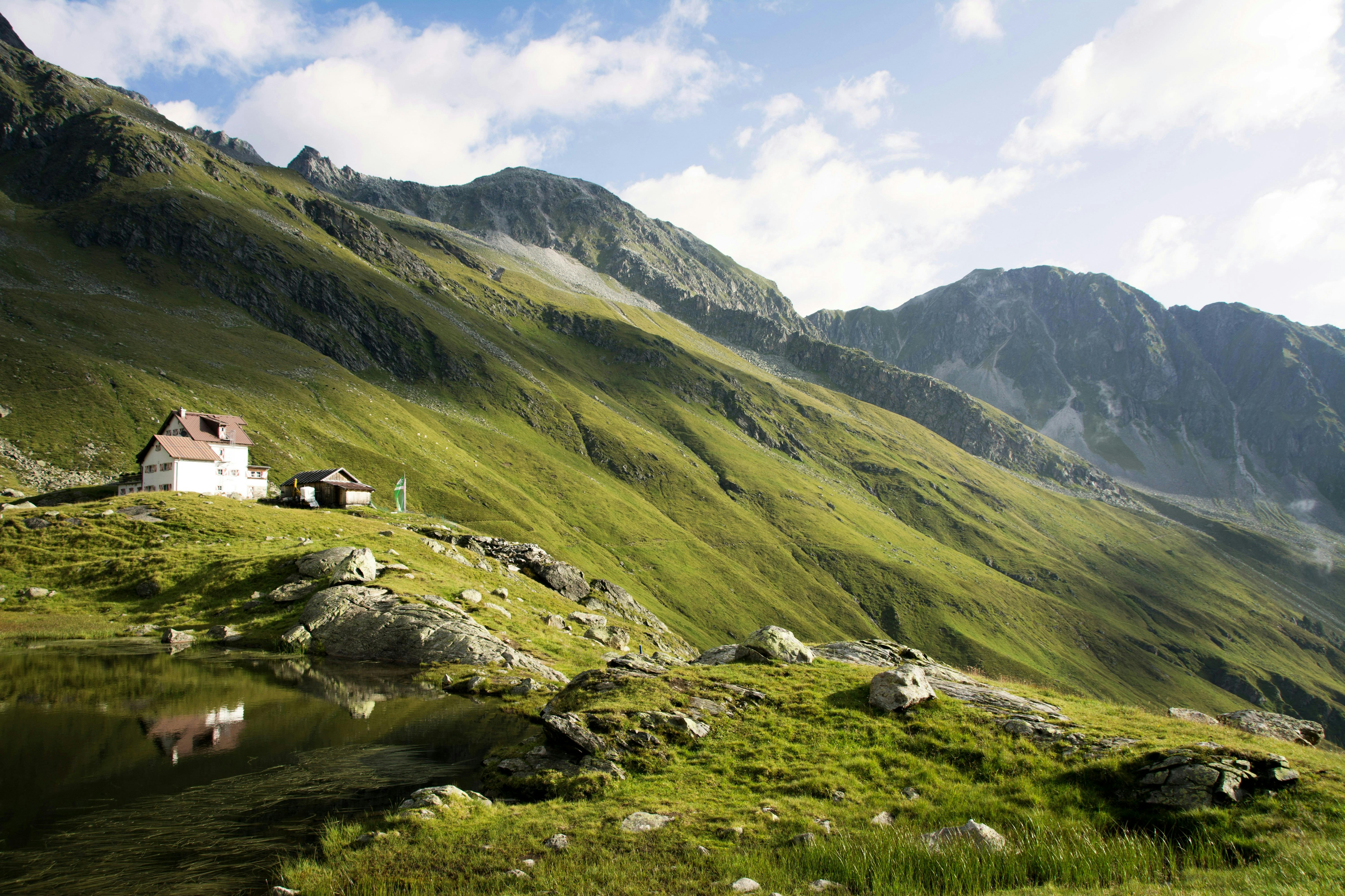 Green verdant mountainside in Austria, with one white house and shed standing alone in the middle of it.