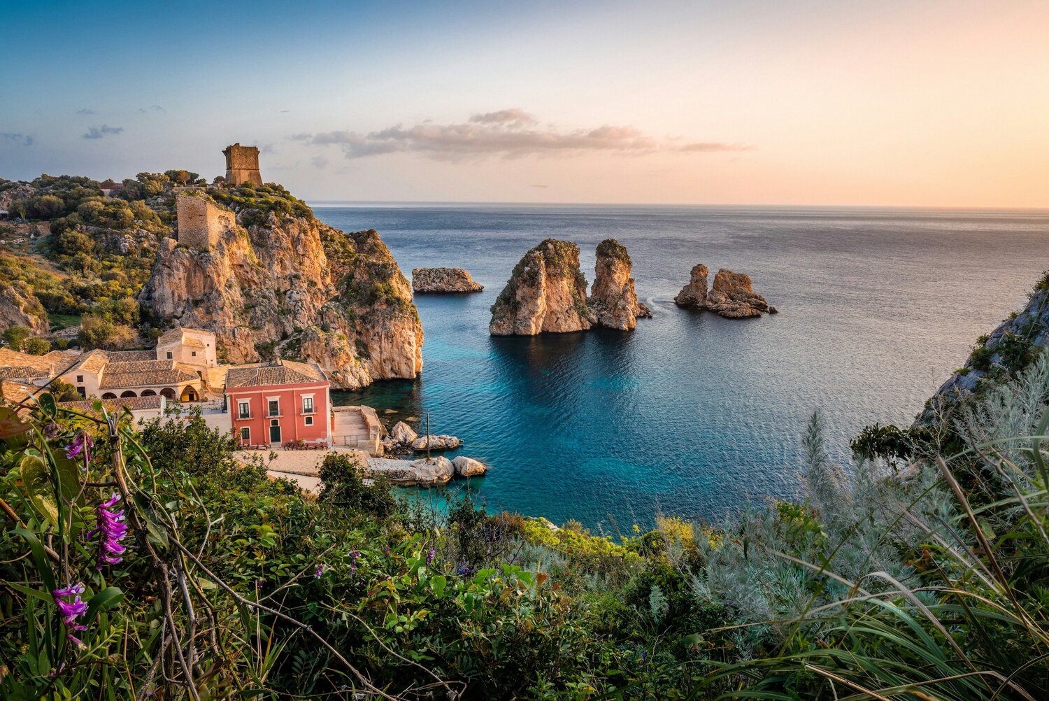 A view from a hilltop on Sicily by train, with green grass and the train station below, you can see the cliffs going into the sea.