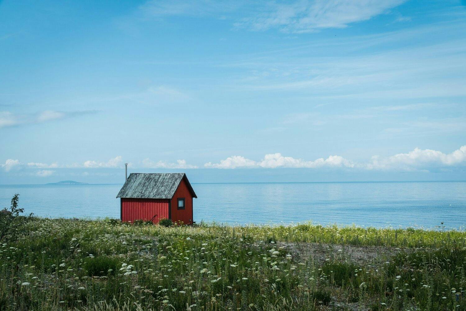 a small red cabin on the lakefront with a green field in the foreground