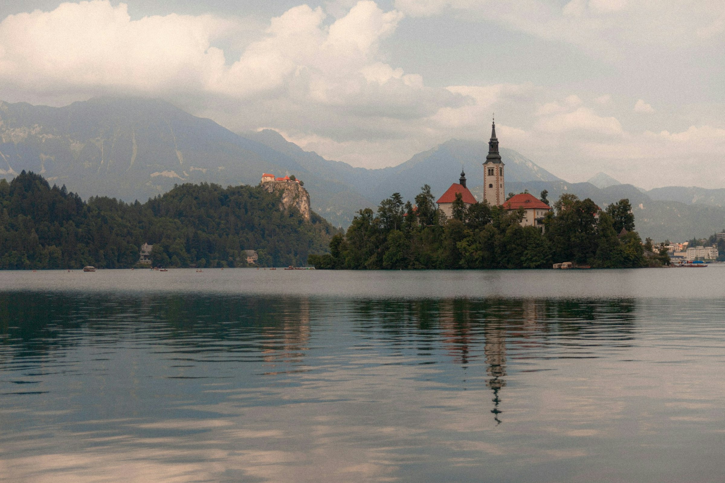 Lake Bled's island church and hilltop castle rise above still water, mountains layered behind.