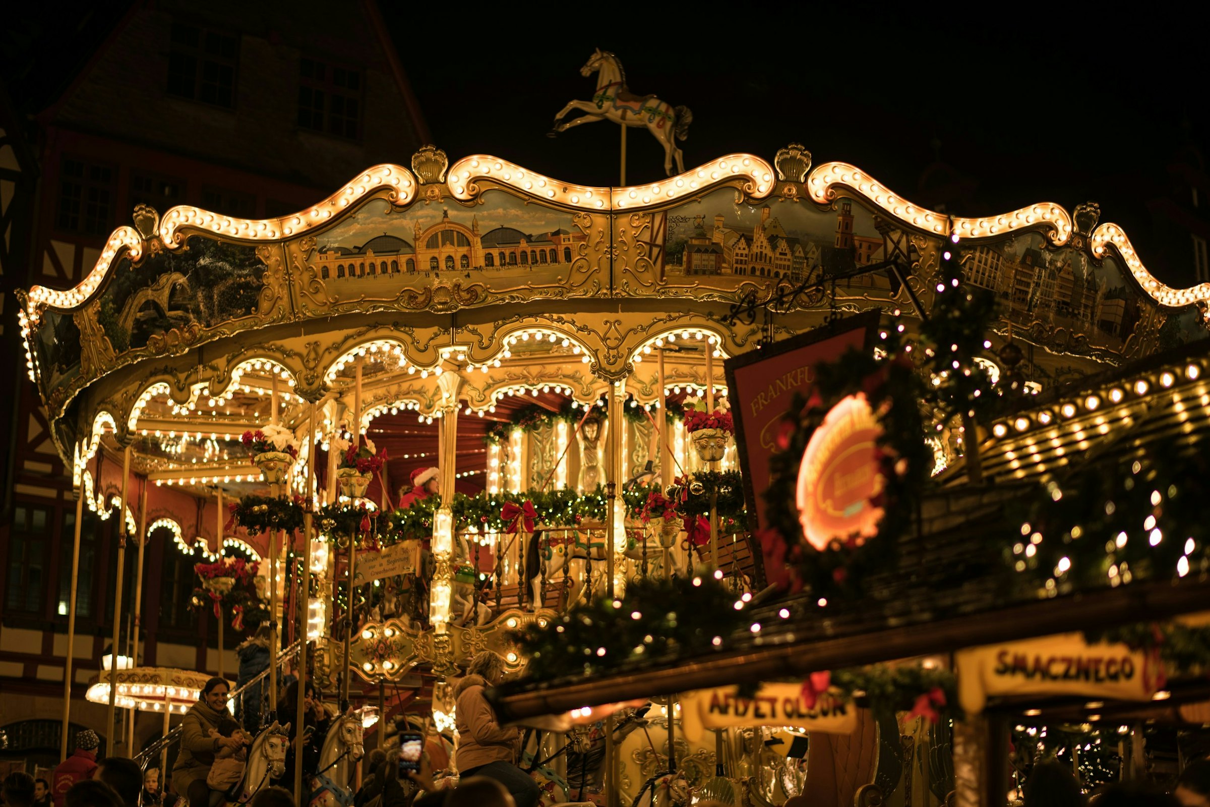 An illuminated carousel glows at night among stalls at a European Christmas market.