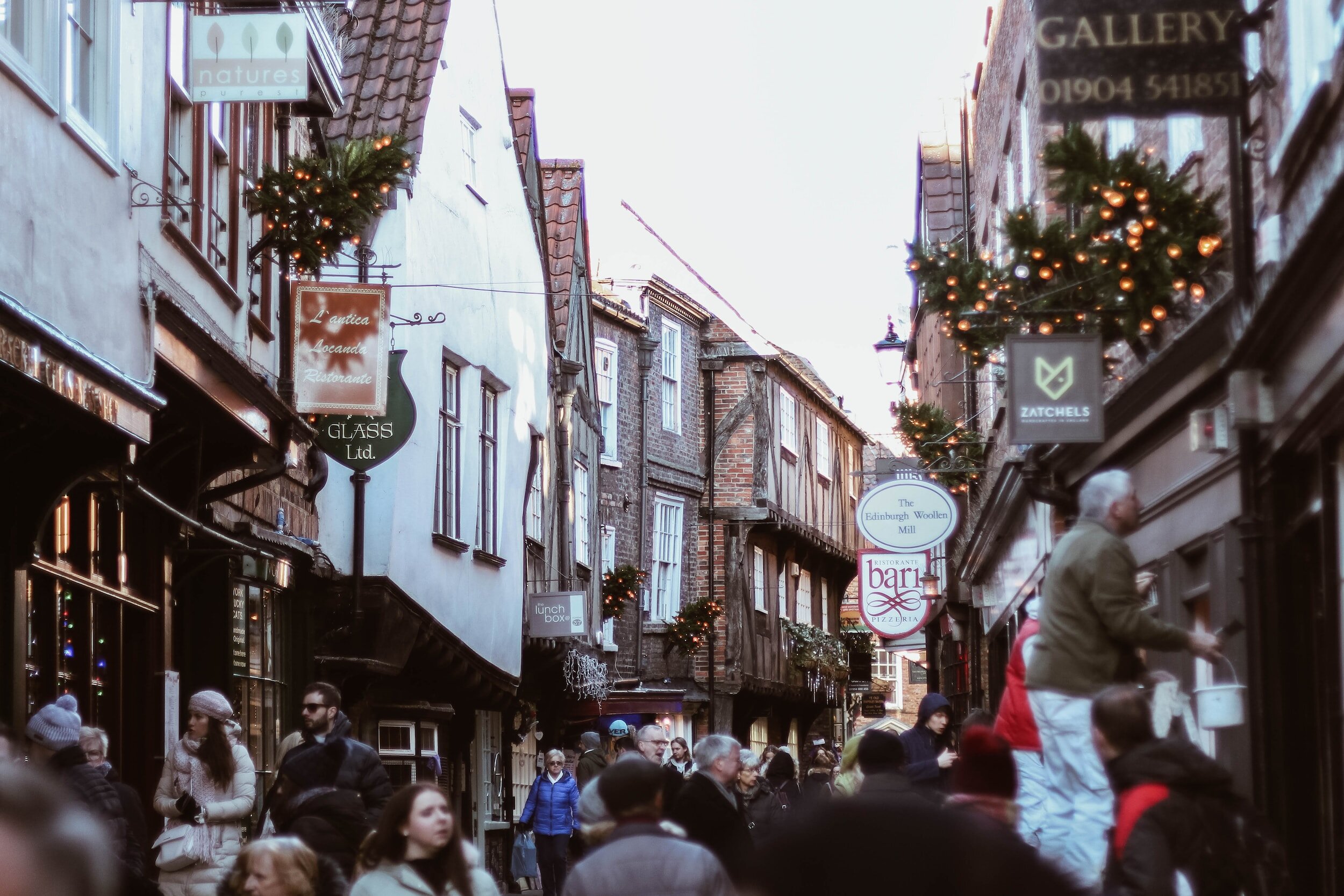 the shambles streets of York at Christmas time, people walking through the small streets with old leaning houses, with old shops decorated with christmas lights.