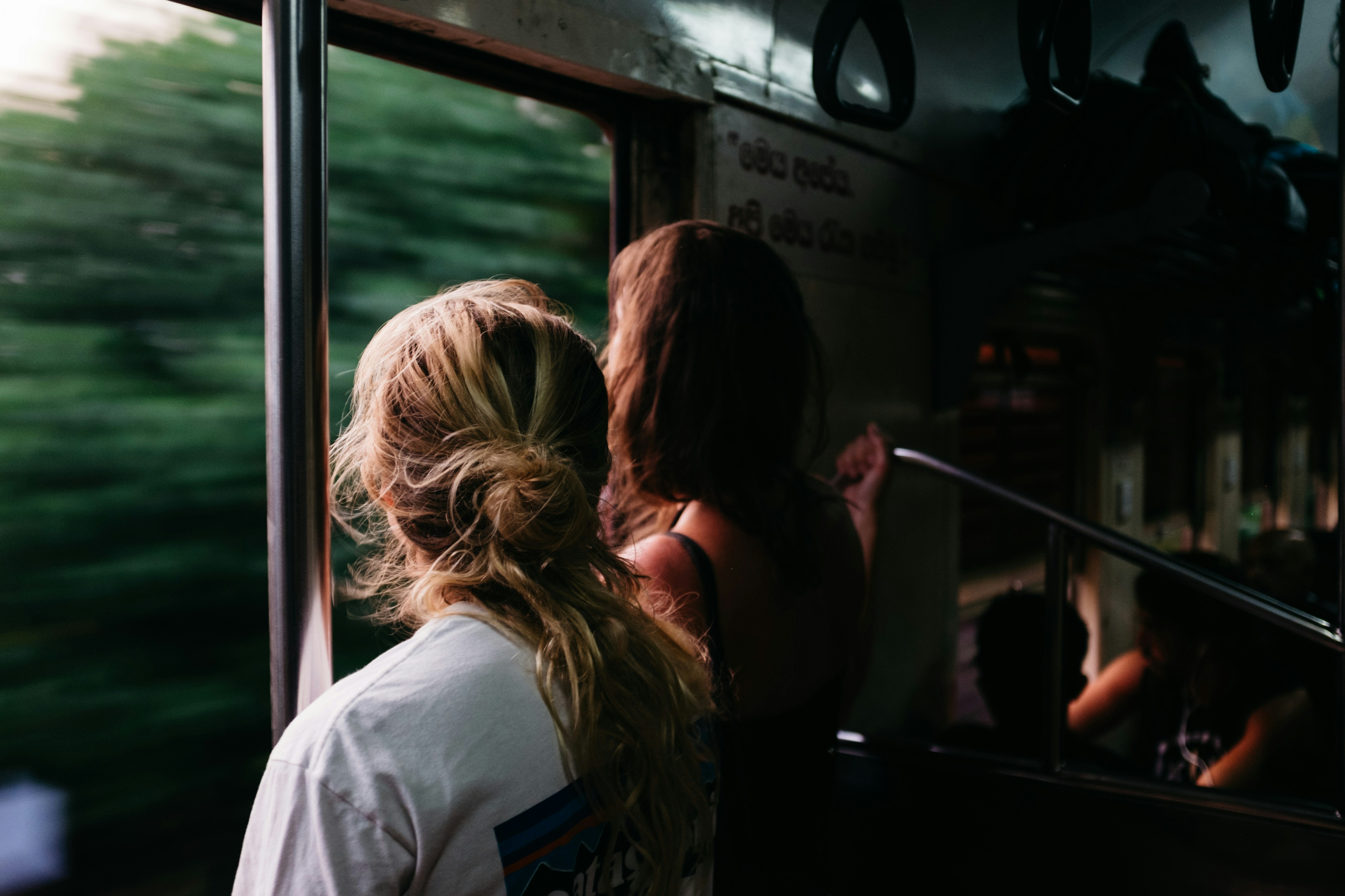 Two people looking out the train window at green trees