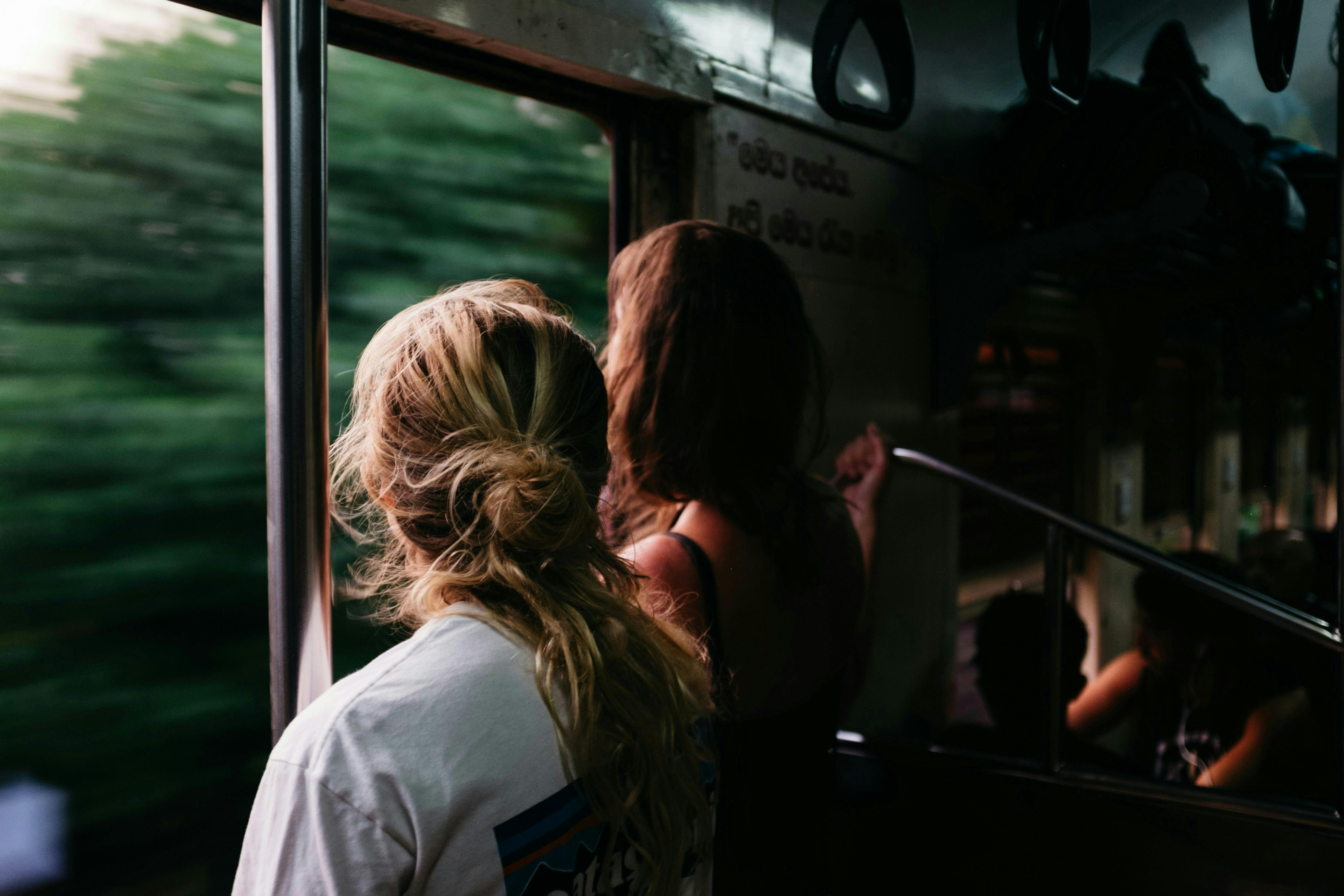 Two people looking out the train window at green trees