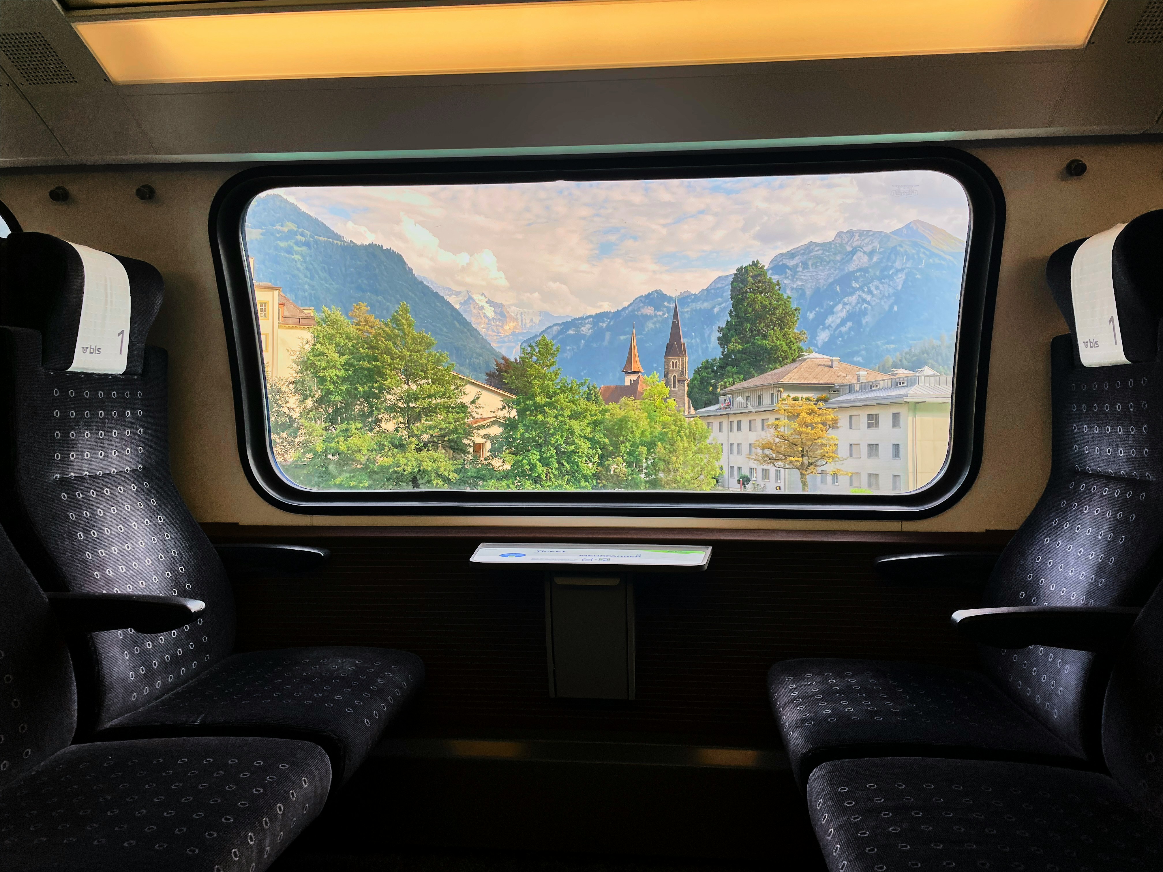 four train chairs with a table and the window view shows a town in front of mountains