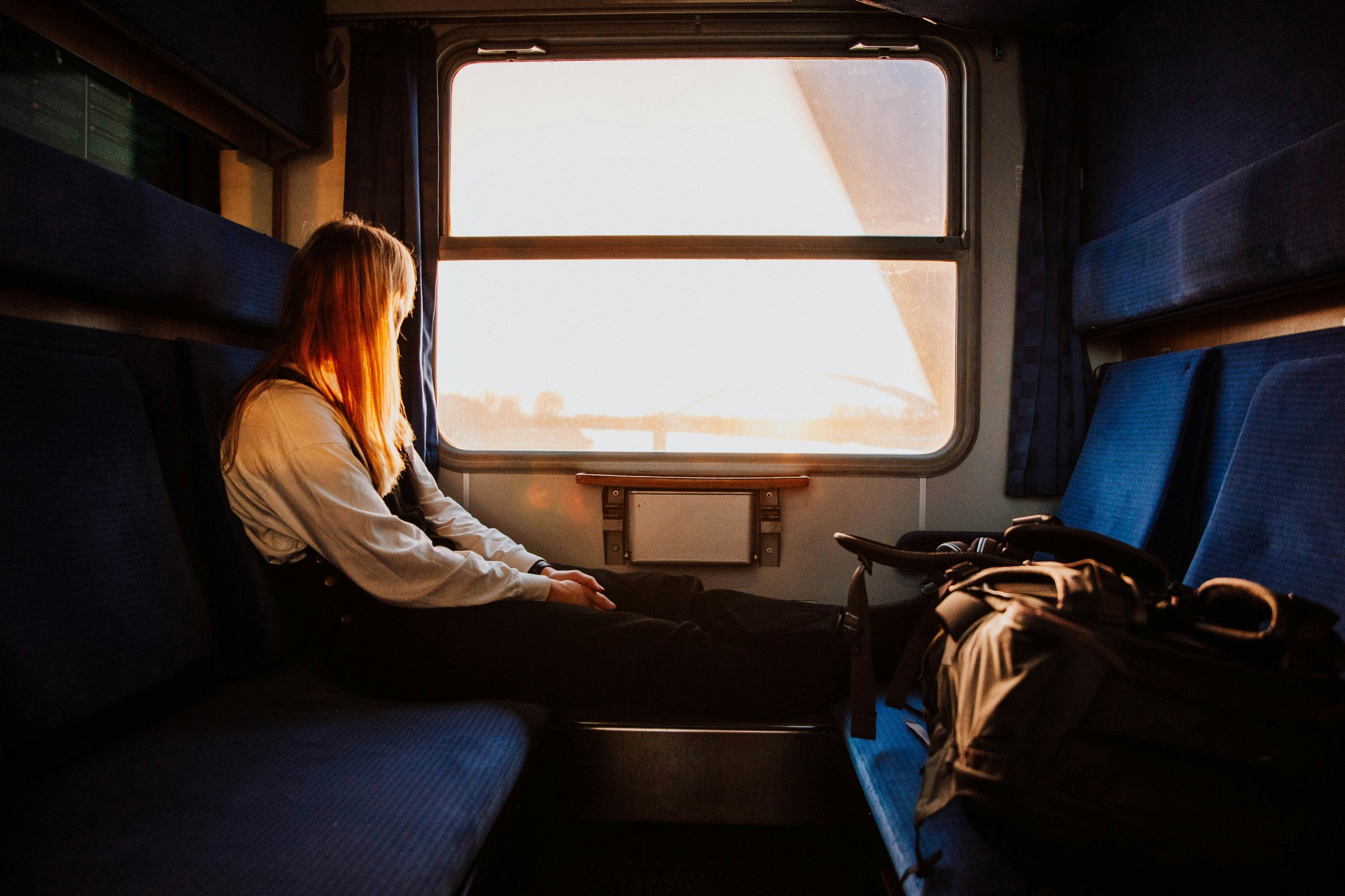 A woman sitting in a train carriage with her feet on the chair in front of her, staring out the window