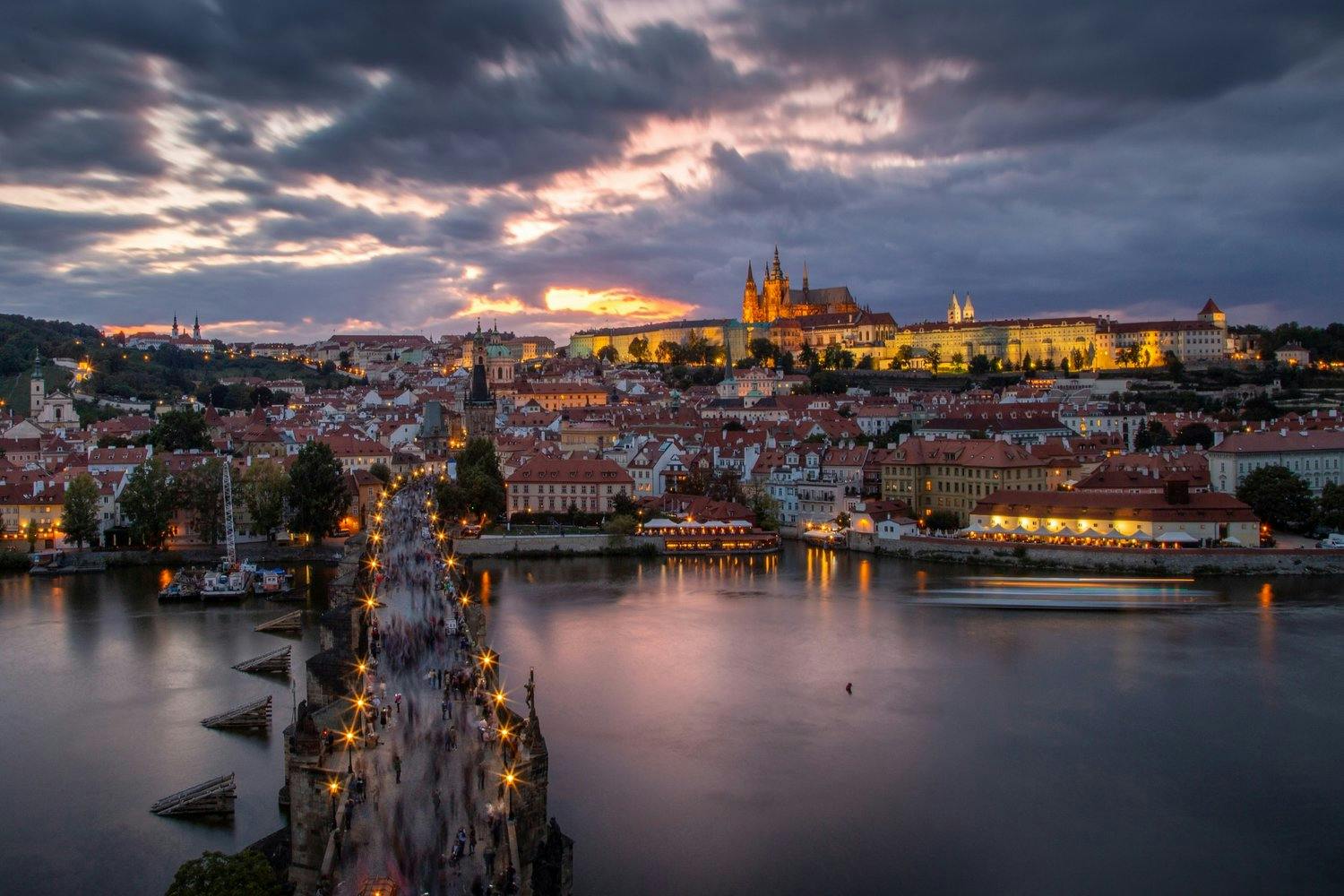 A veiew of the Charles bridge in Prague at dusk, lights shining on the houses and the castle on the hill