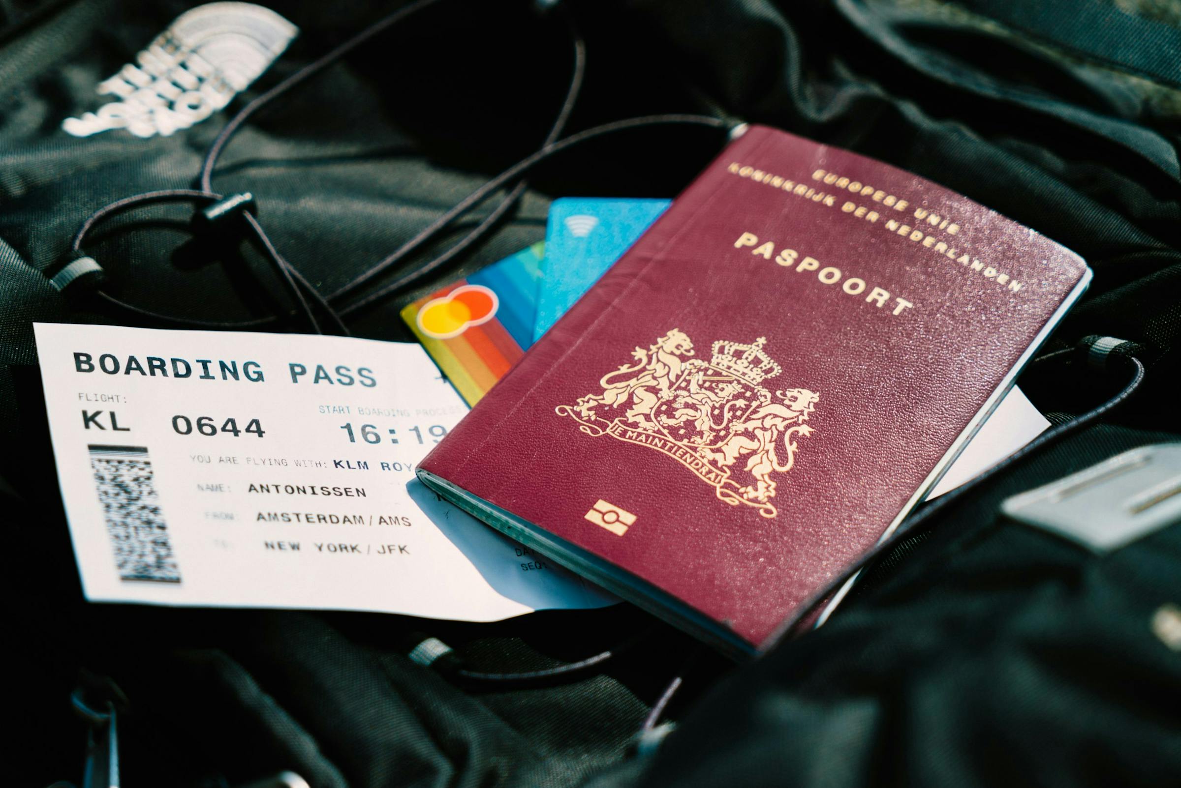 A Dutch passport and KLM boarding pass for an Amsterdam to New York flight, next to bank cards.