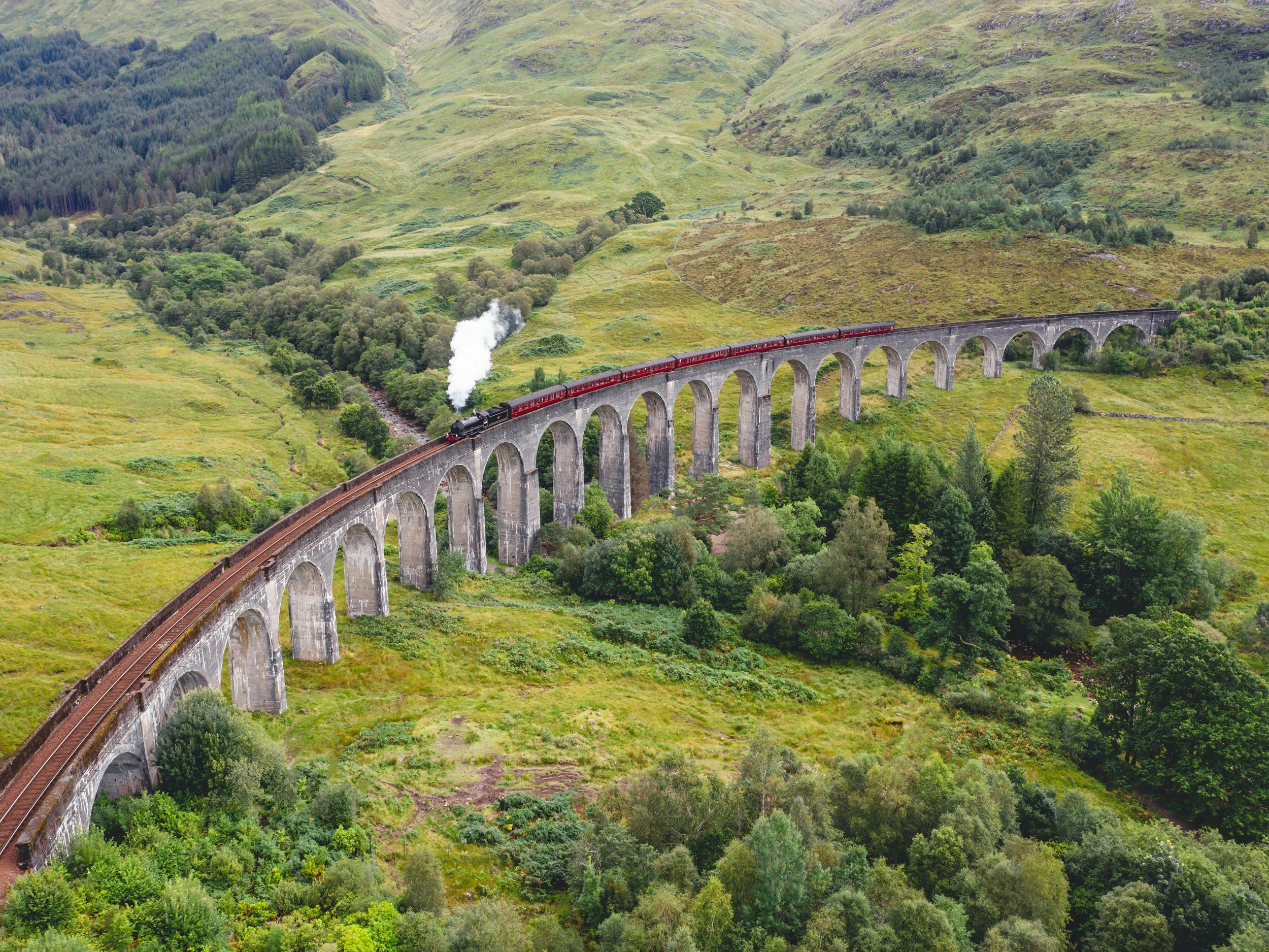 looking down on a viaduct with a steam train traversing the scottish countryside