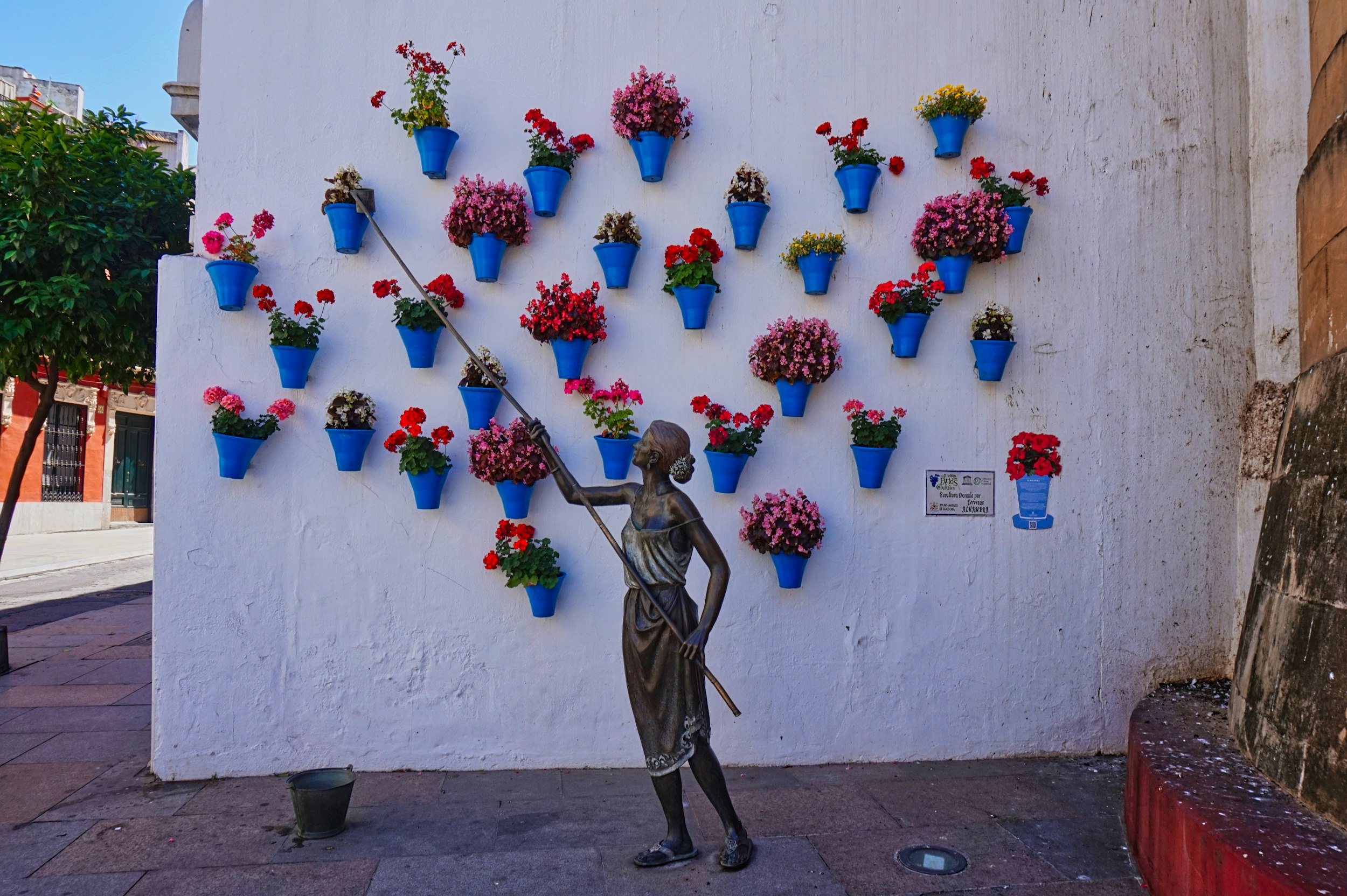 A statue of a woman holding a stick in front of a wall with vases