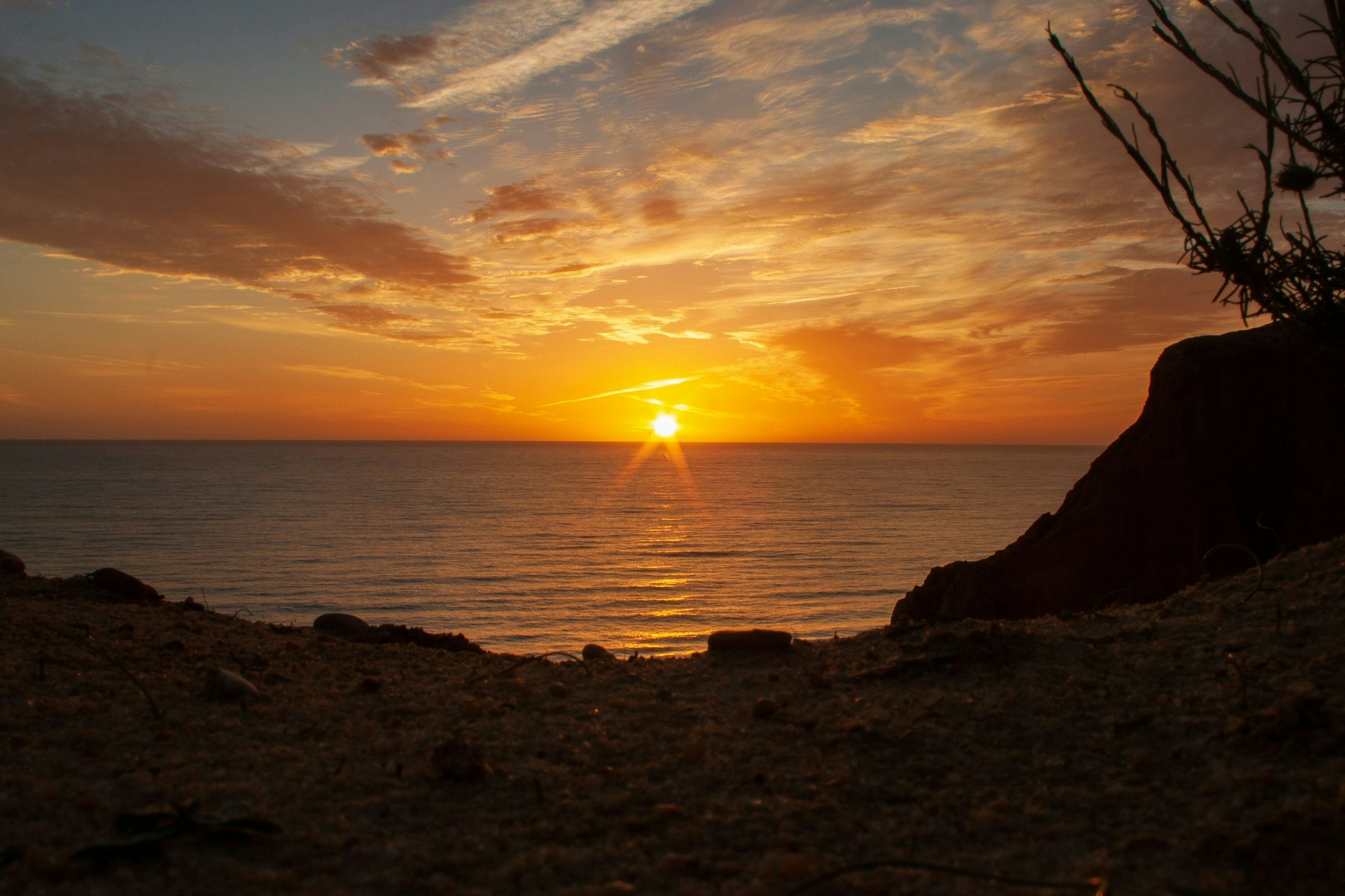 silhouet van persoon staand op rots bij zee tijdens zonsondergang