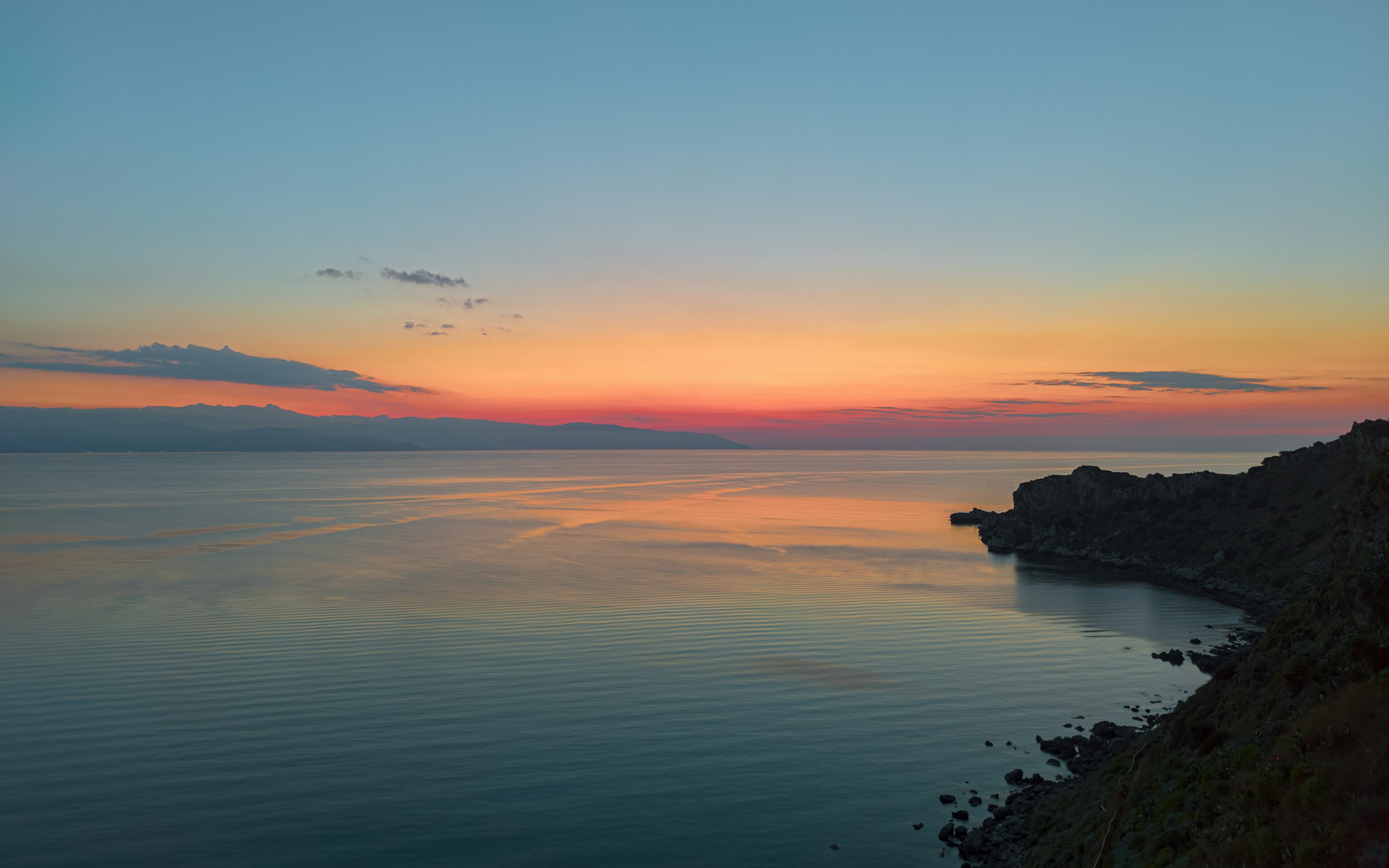 a sunset over a body of water with mountains in the background