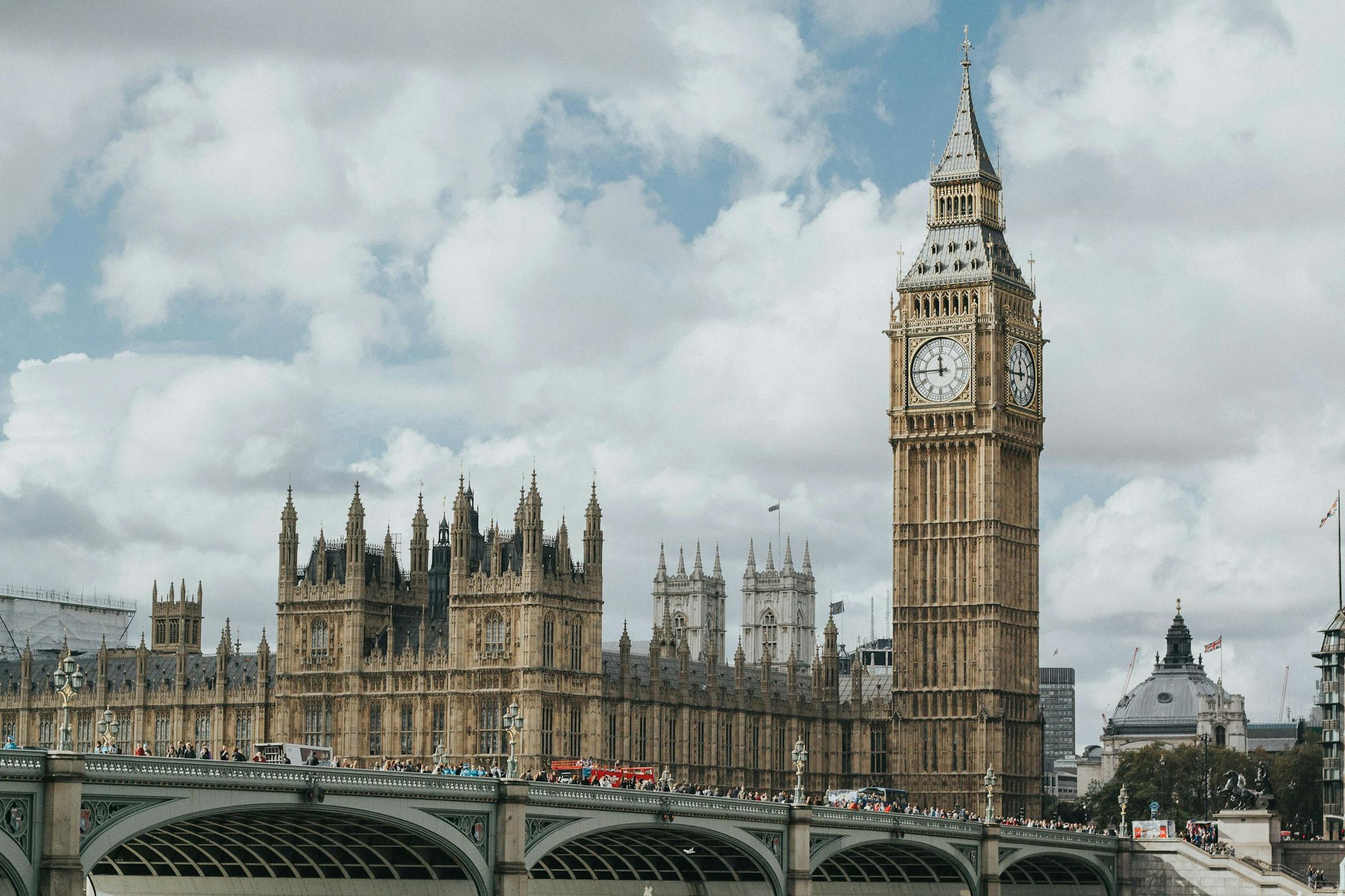 Big Ben and the Houses of Parliament rise beside Westminster Bridge under a cloudy London sky.