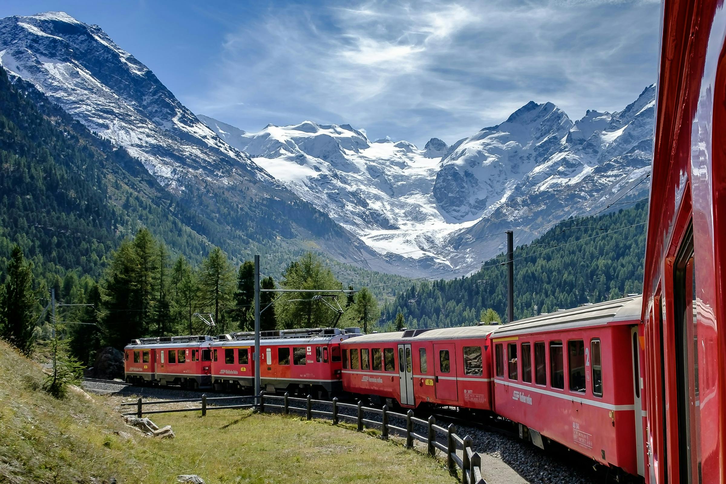 Red Rhaetian Railway train winding along a mountainside beneath a glacier in the Swiss Alps