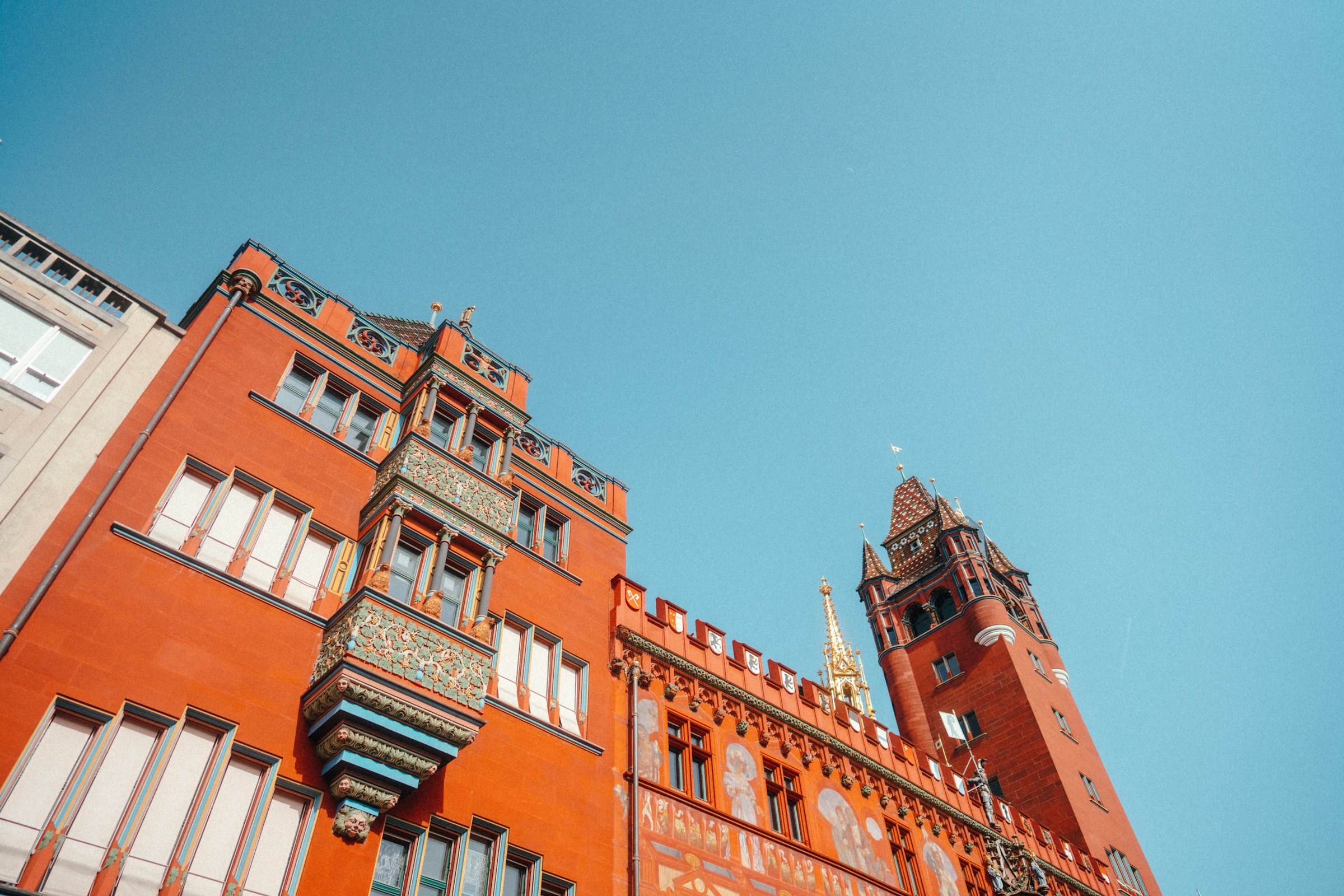 An ornate red sandstone building with a decorated tower and gilded spire stands under a clear blue sky.