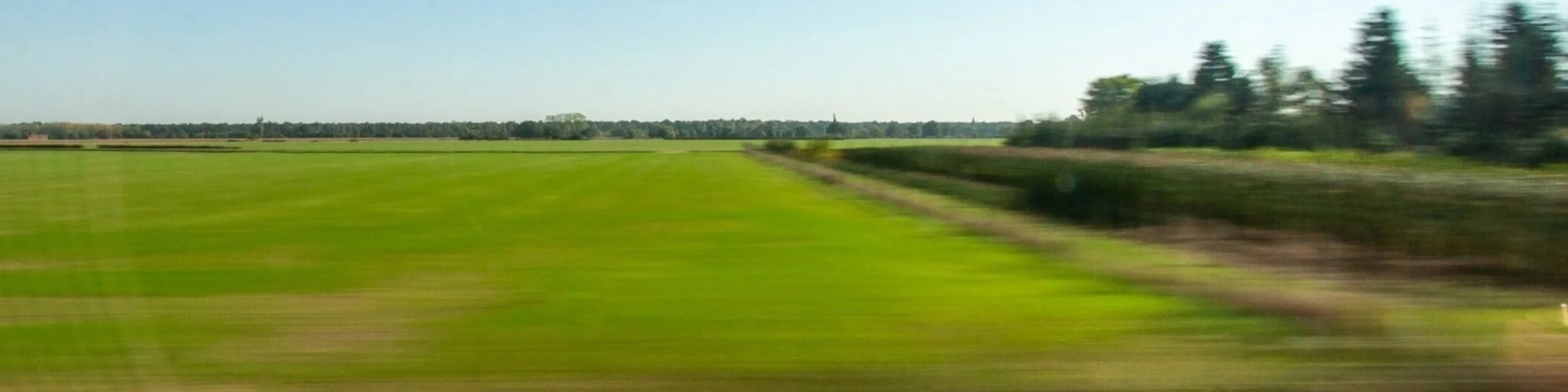 Blurred green fields and a hedgerow rush past, viewed from a moving train window.