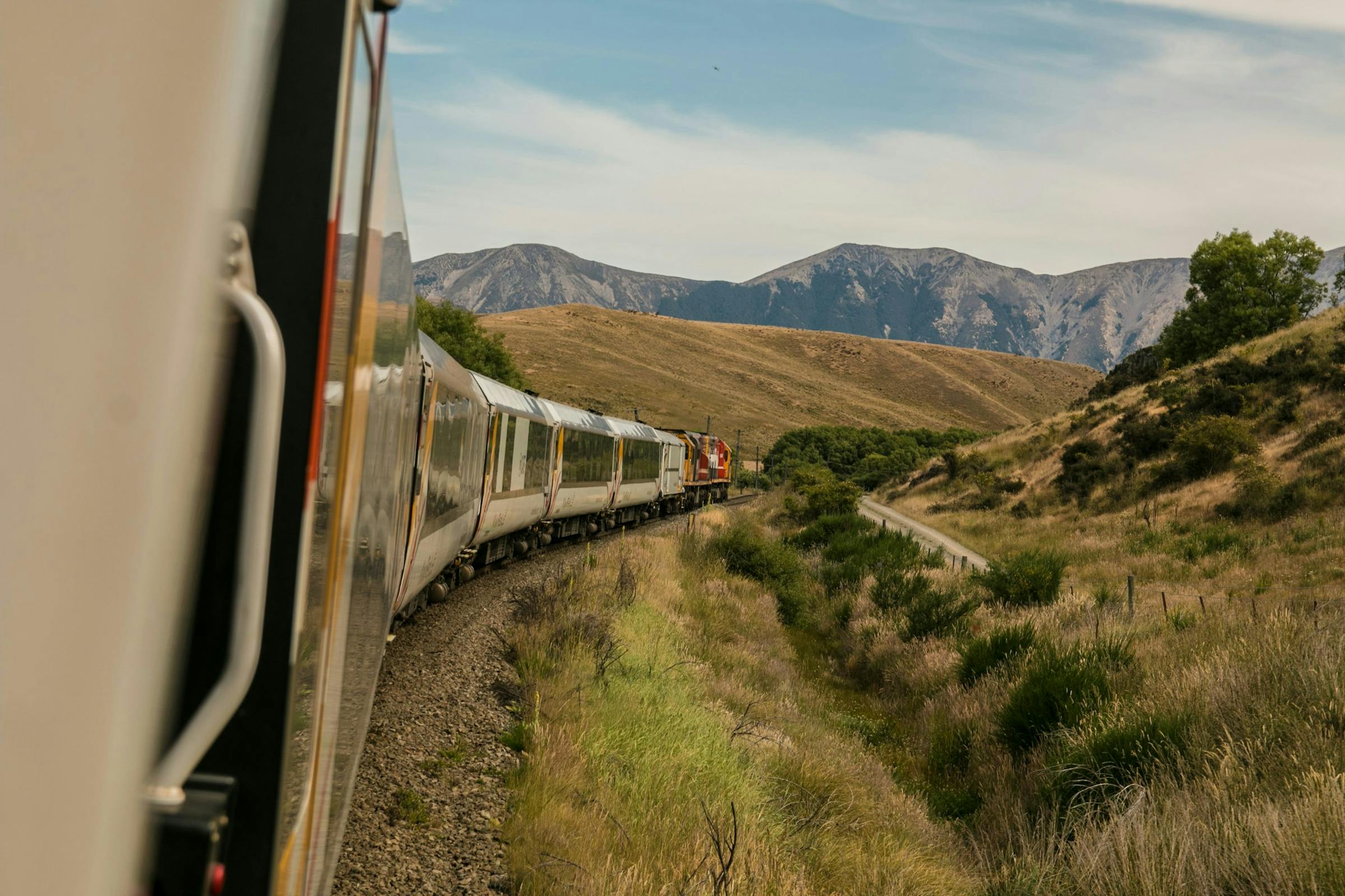 White train with a red locomotive curving along a track through dry hills and mountains.