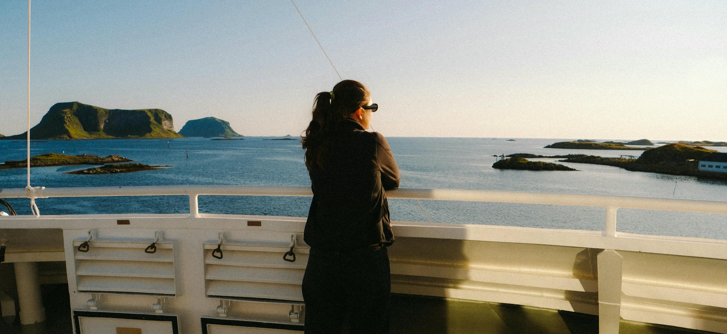 A ferry passenger looks out at small green islands scattered across a calm coastal sea.