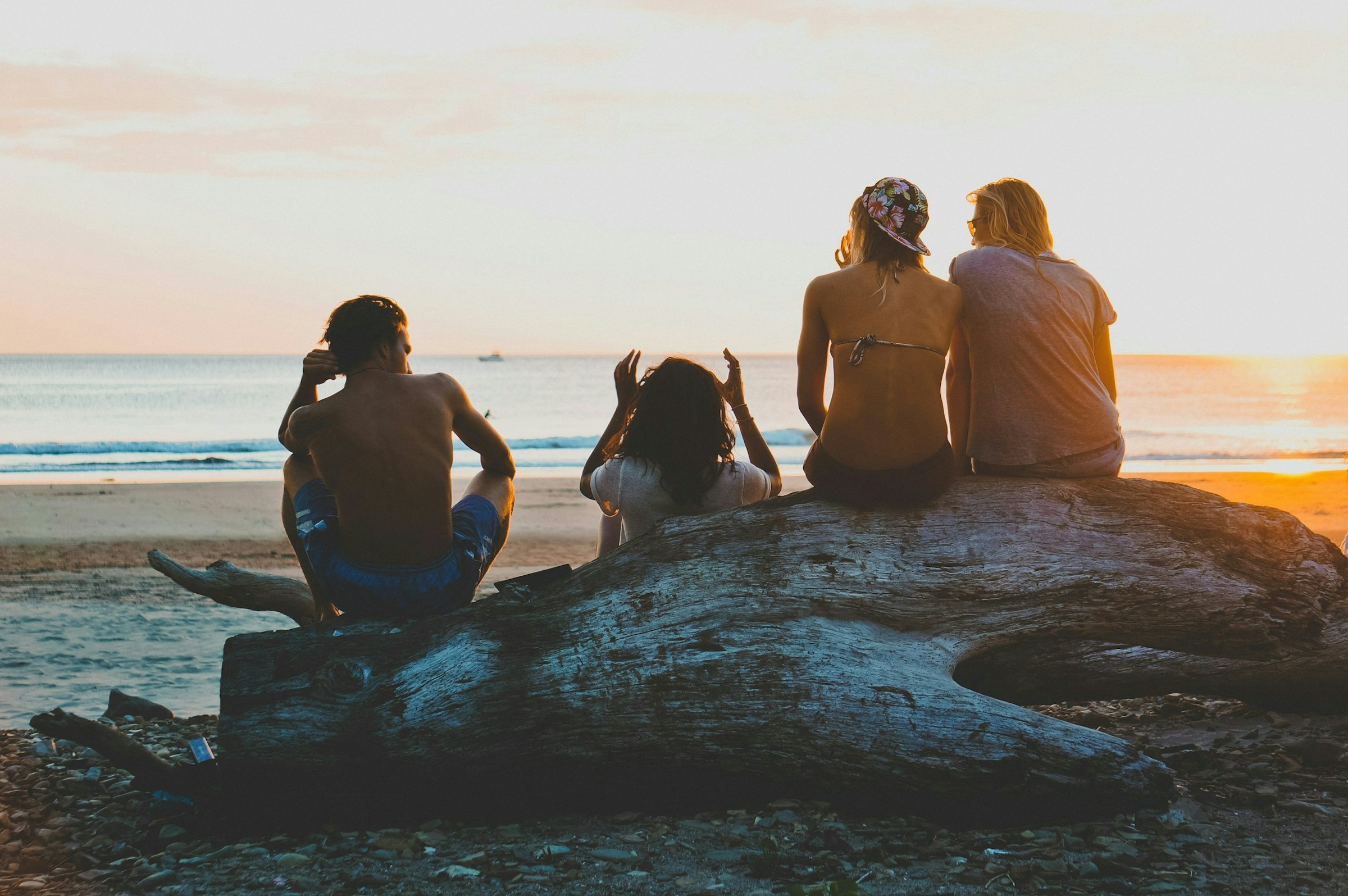 3 women sitting on rock in beach during daytime