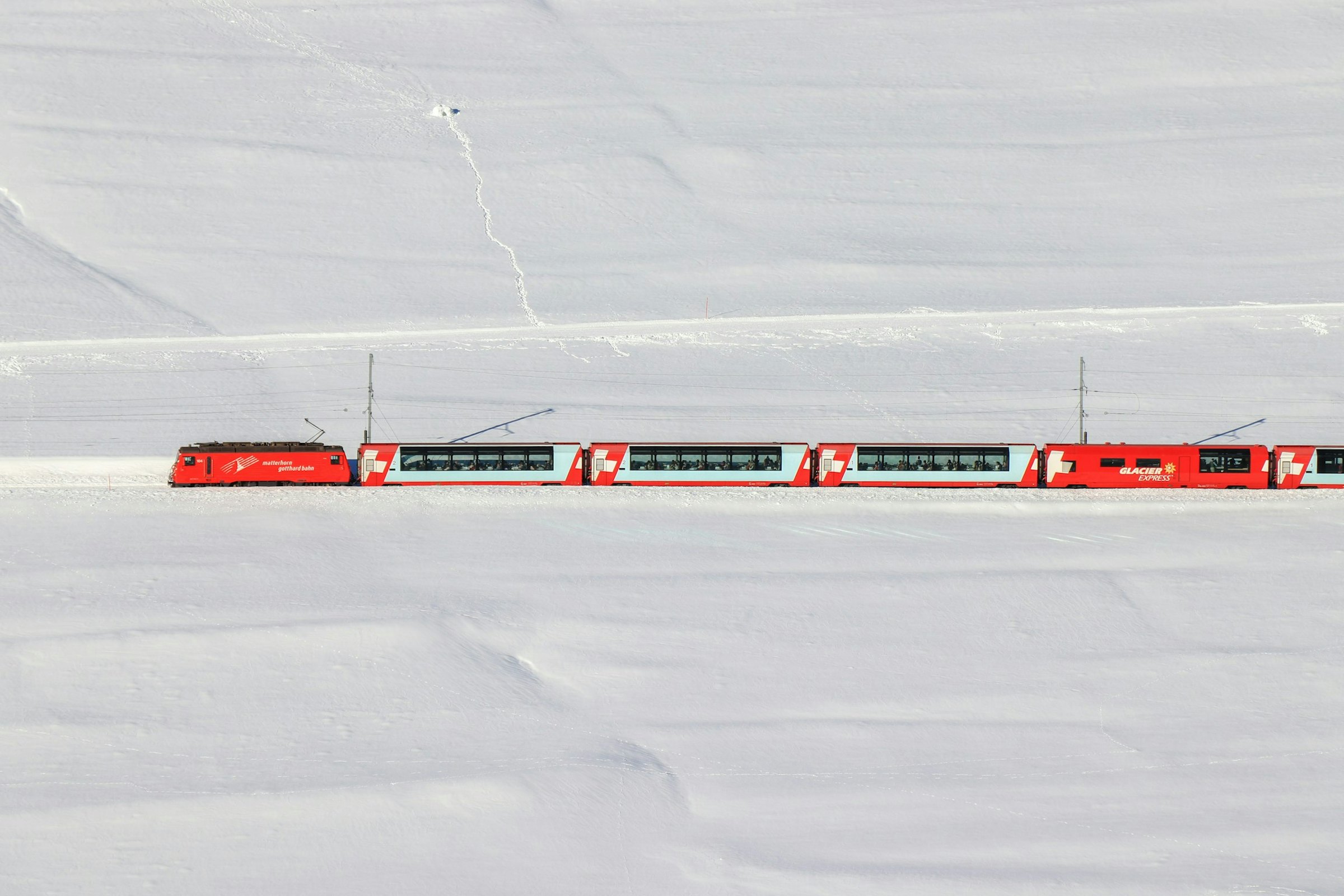 The red Glacier Express train crosses a vast snow-covered plain in the Swiss Alps.