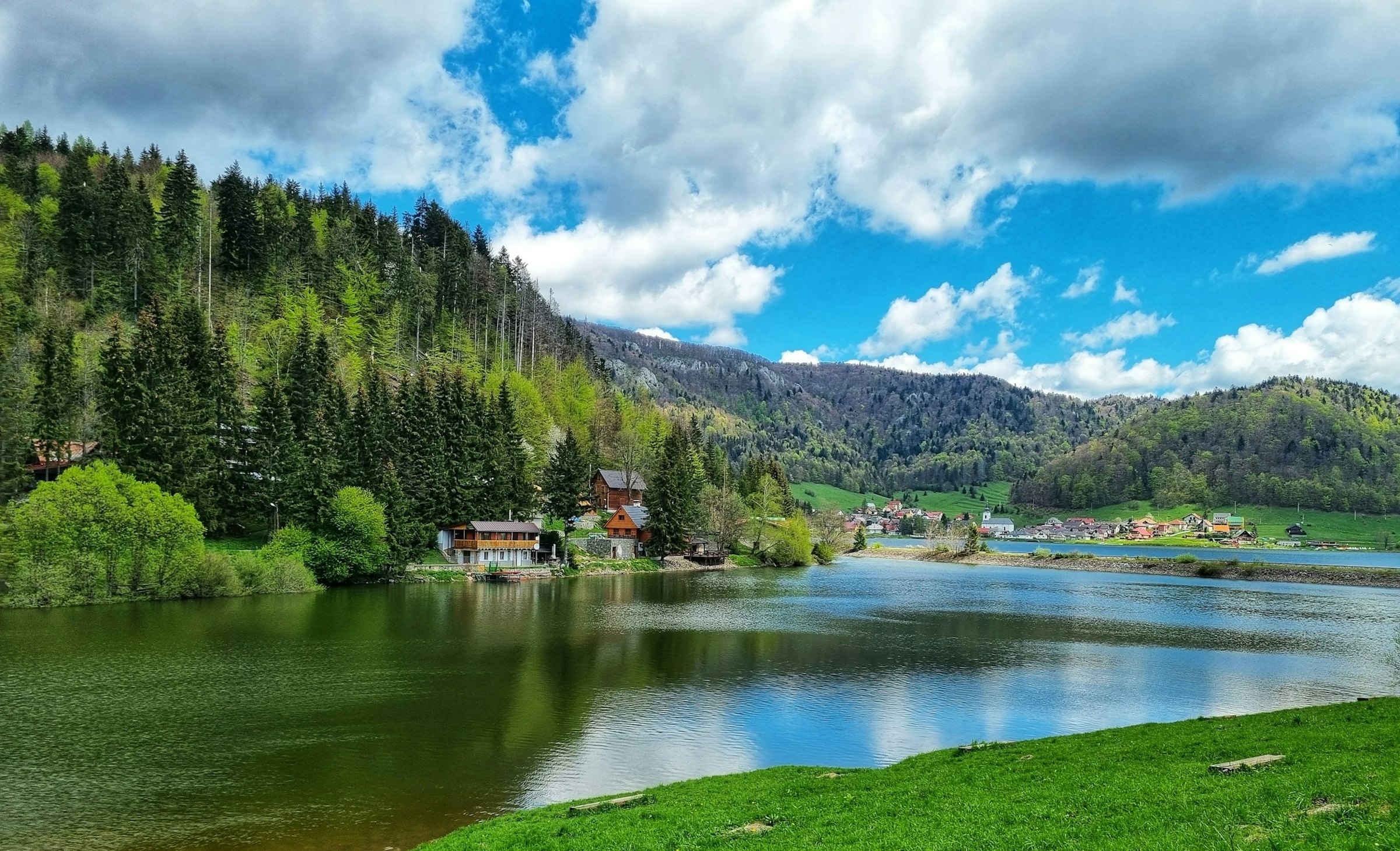 Calm lake ringed by forested hills, a wooden lakeside house in the foreground, rural Slovakia