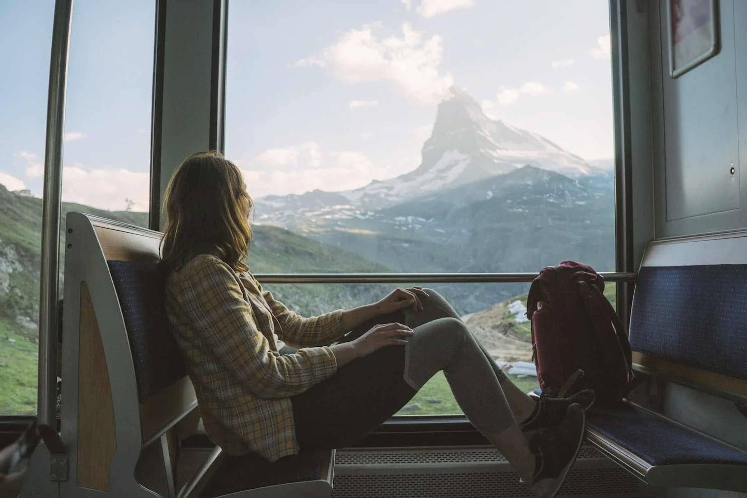 A traveller relaxes by a train window overlooking the snow-capped peak of the Matterhorn.