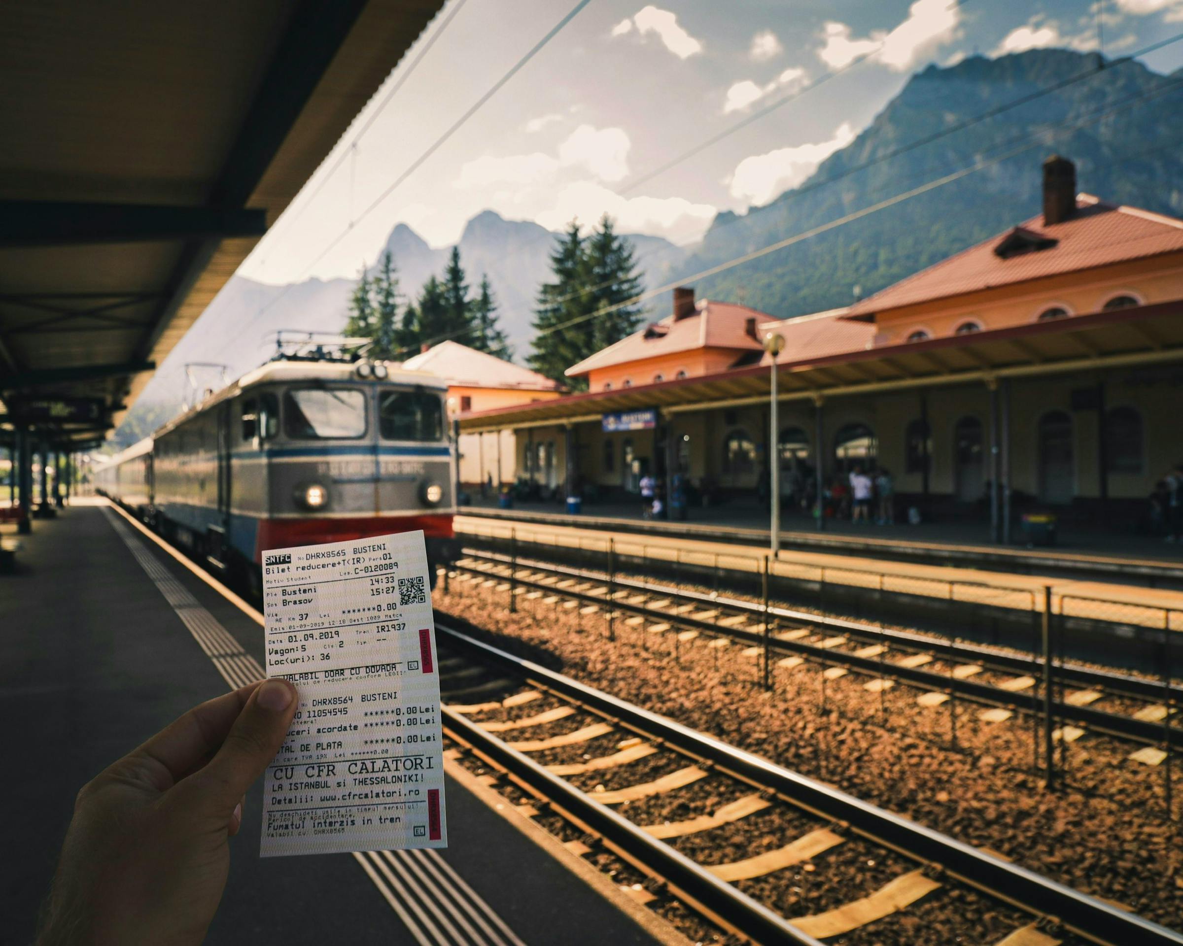 A traveller holds paper train tickets on a mountain station platform in Romania.
