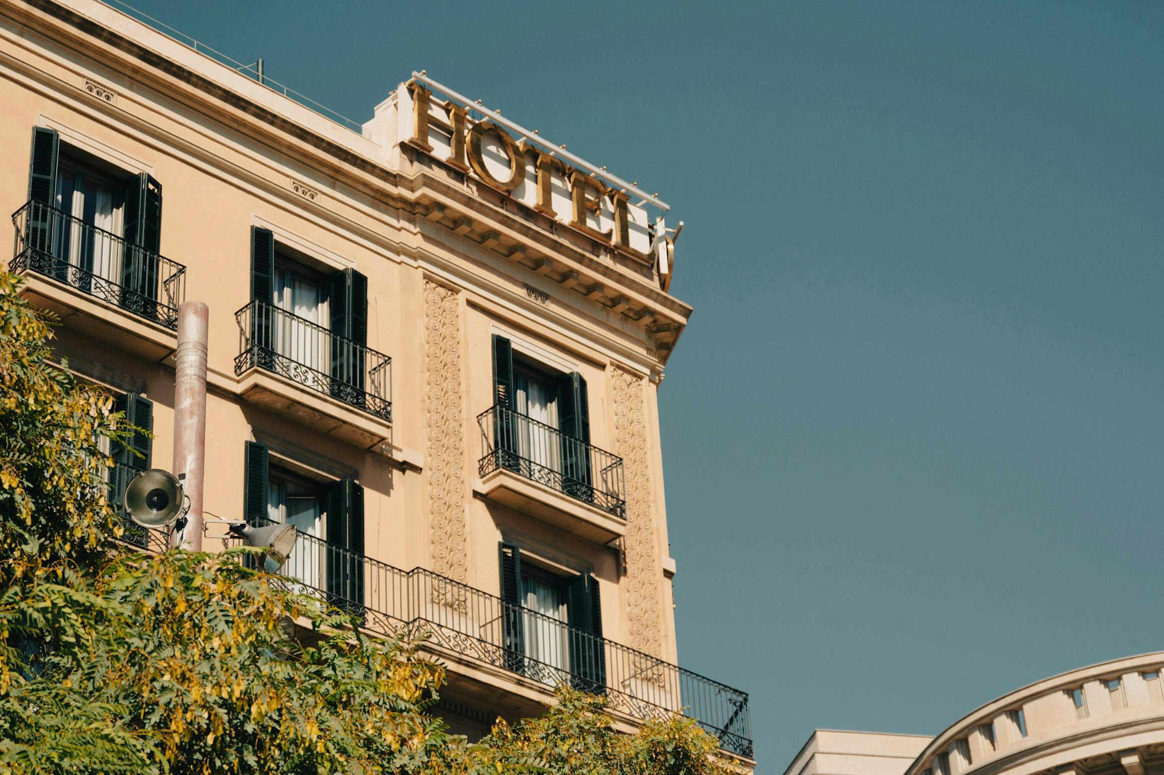 An ornate European hotel facade with wrought-iron balconies beneath a gold rooftop sign.