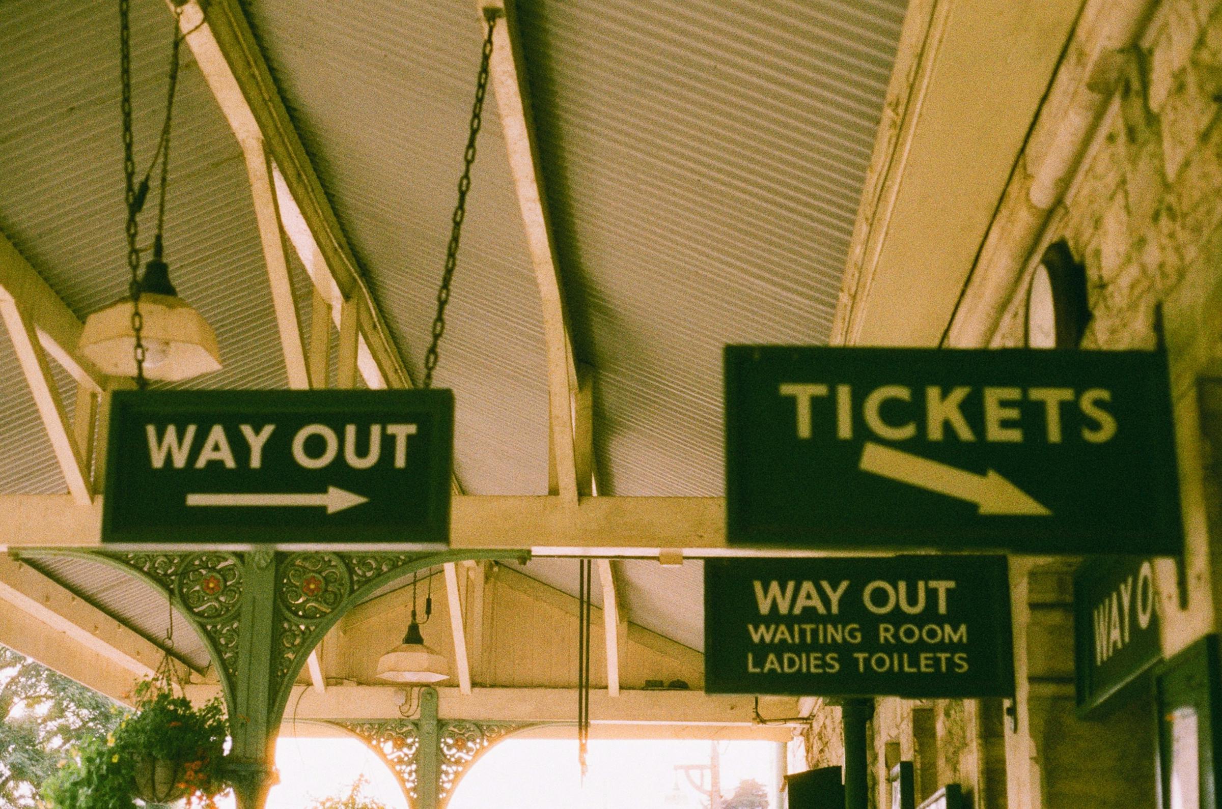 Vintage green station signs reading Tickets and Way Out hang beneath a covered platform roof.