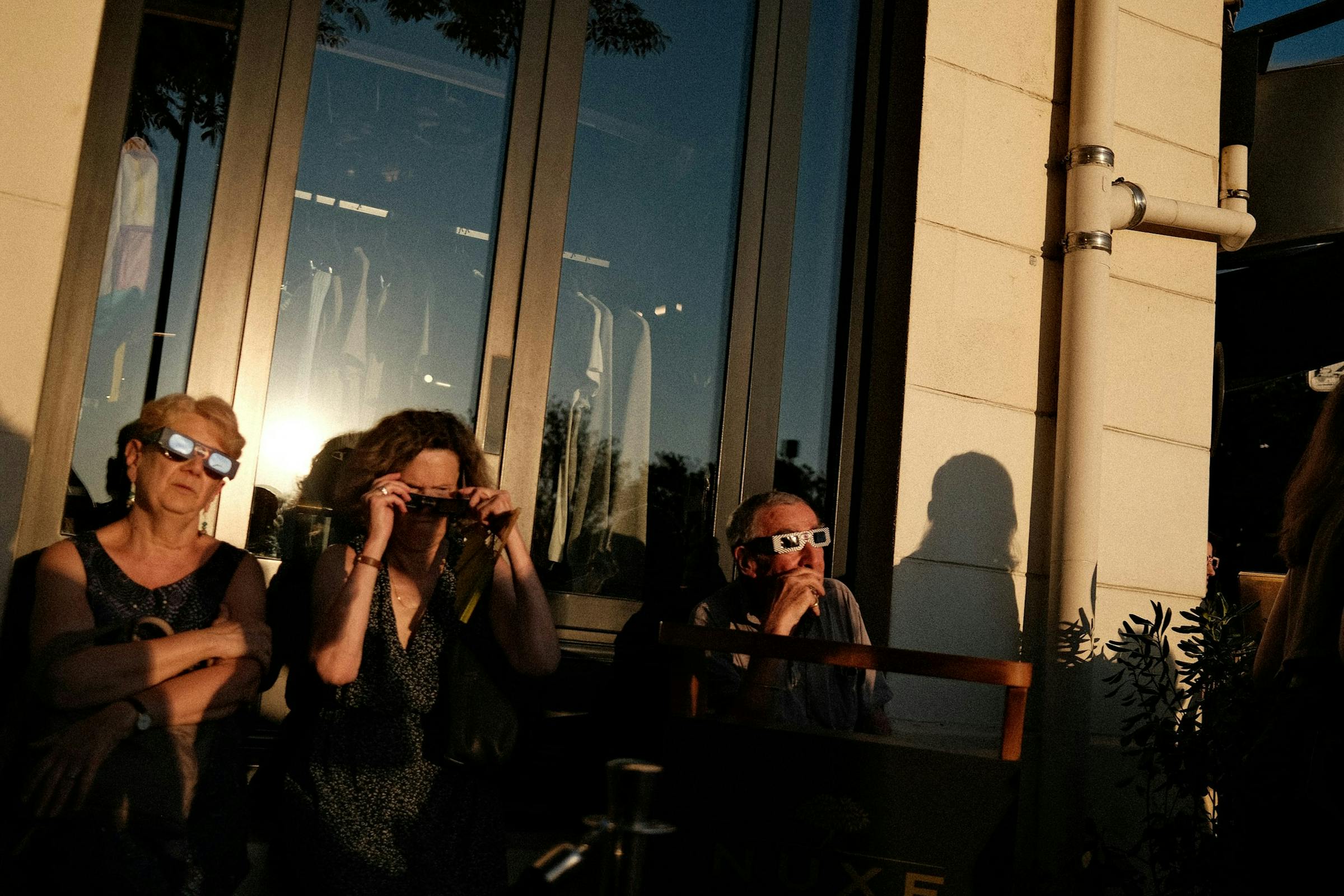 Three people wearing eclipse glasses in the warm light of a late afternoon