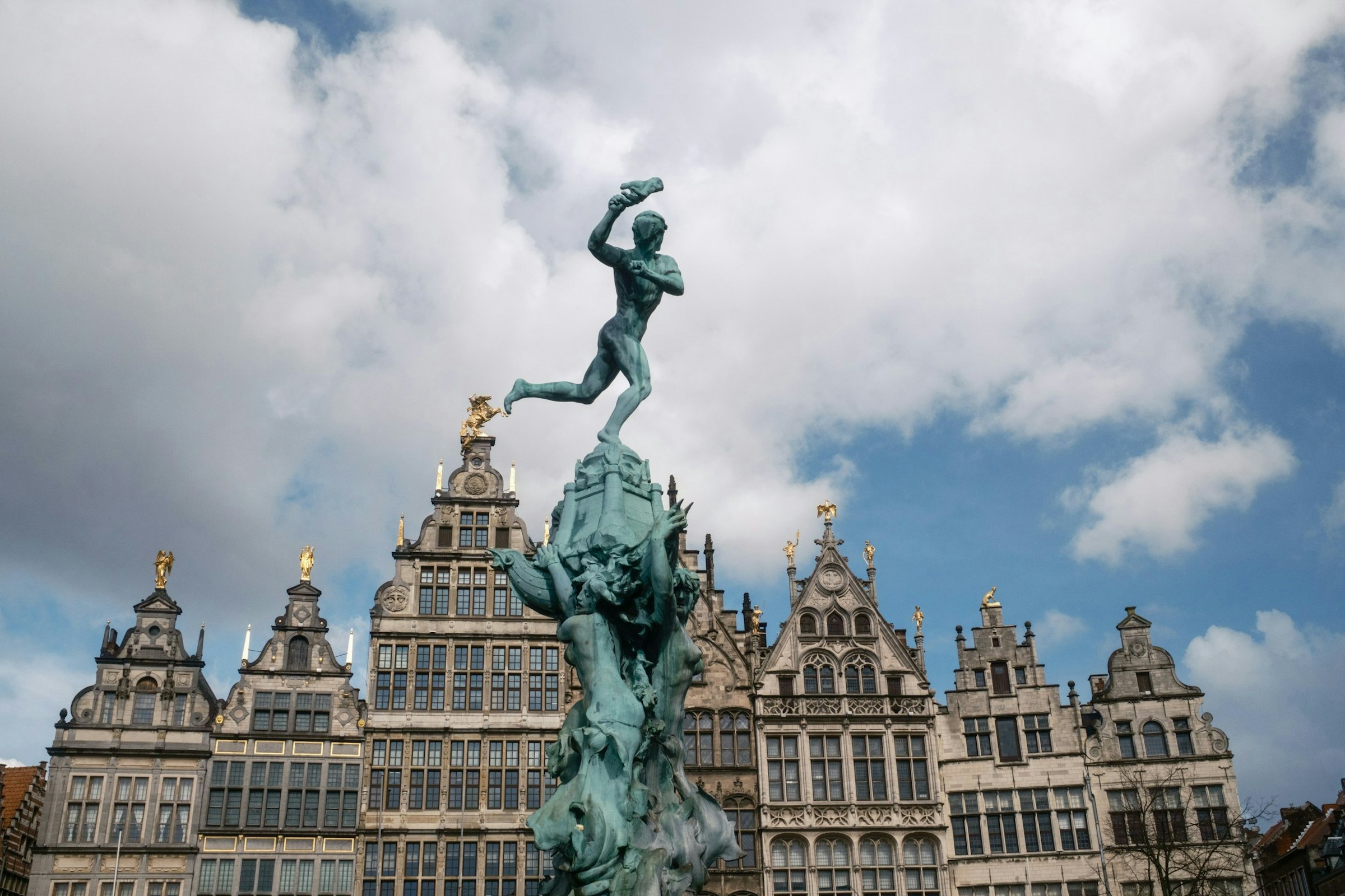 A bronze statue stands atop a fountain with buildings behind