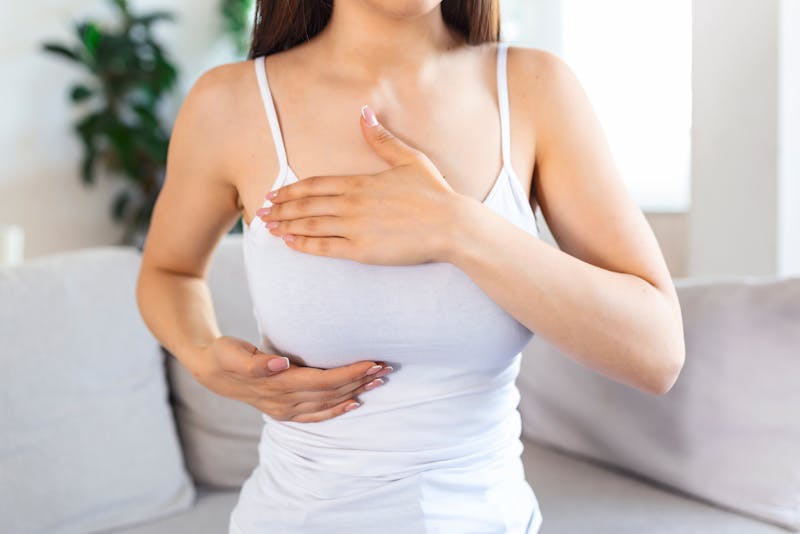 a woman wearing a white tank top checking her breast