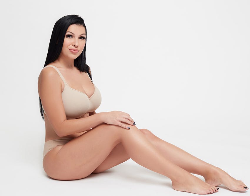 Black-haired woman sitting on the ground posing in tan undergarments