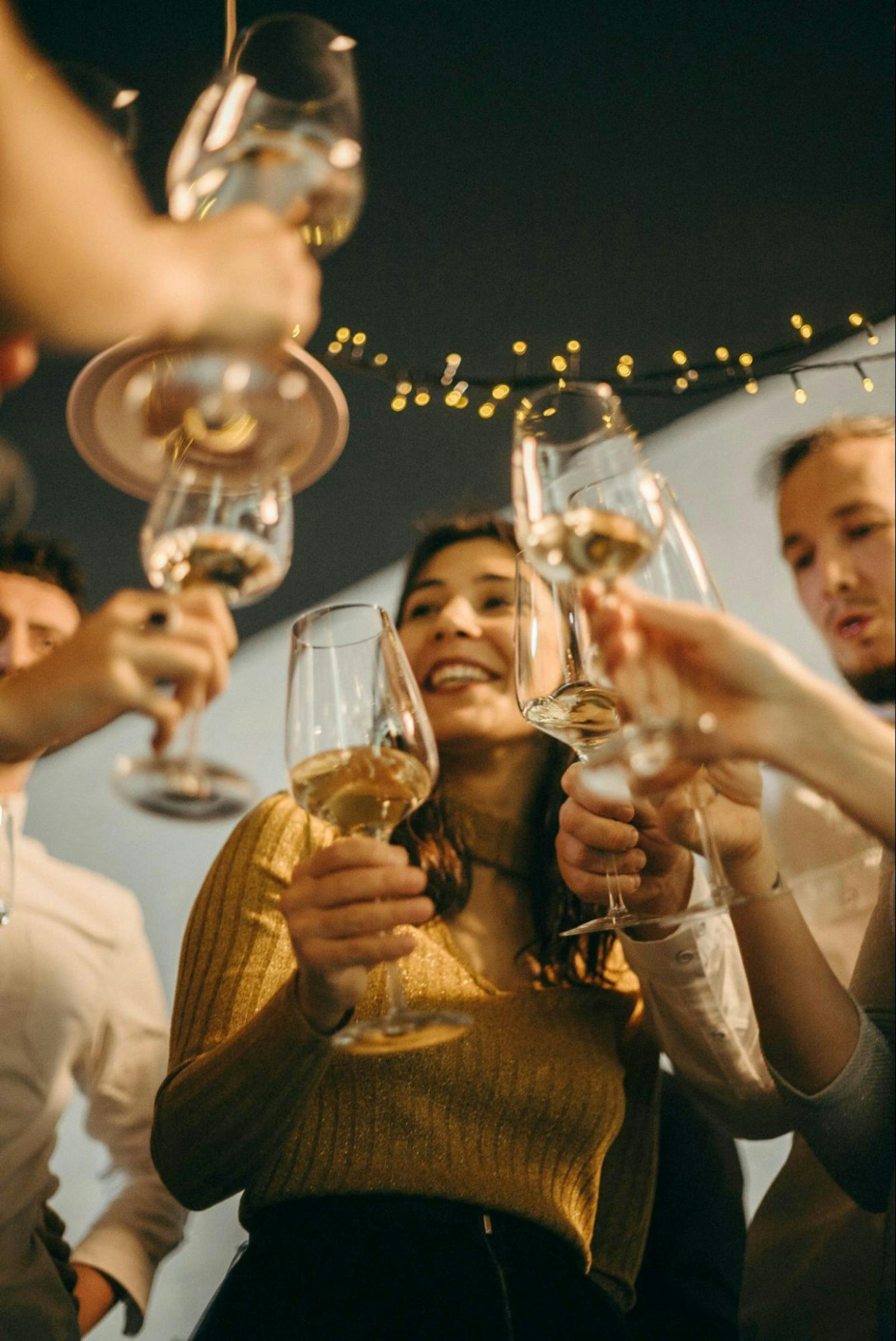 A group of friends raising wine glasses for a toast at a festive celebration with warm lighting.