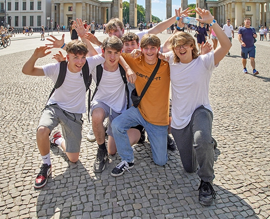 A group of boys crouch beneath the Brandenburg Gate in Berlin, waving at the camera