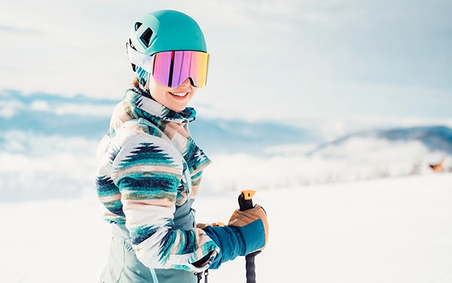 Young girl in ski gear looks over shoulder, smiling, with mountains in background