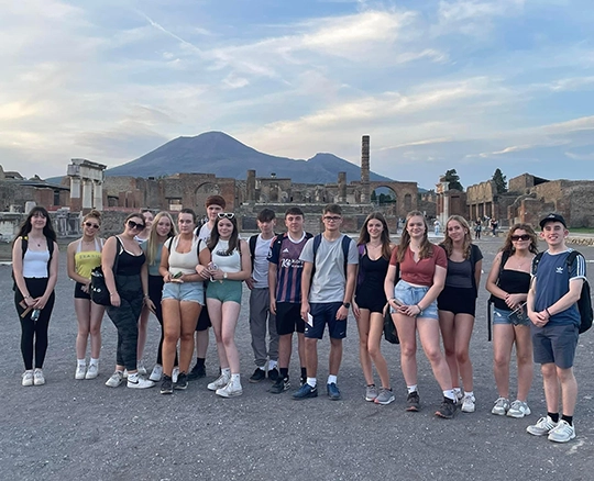 A group of teenagers stand in front of Pompeii's ruins with Mount Vesuvius behind