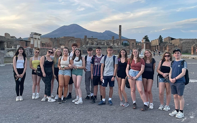 A group of teenagers stand in front of Pompeii's ruins with Mount Vesuvius behind