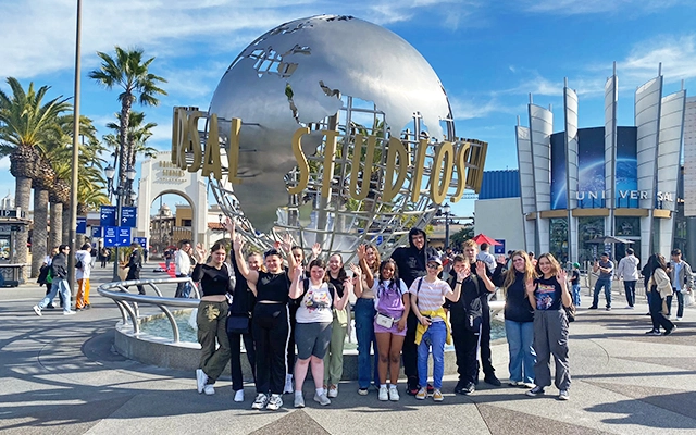 A group of young people stand in front of the Universal Studios globe with their arms raised